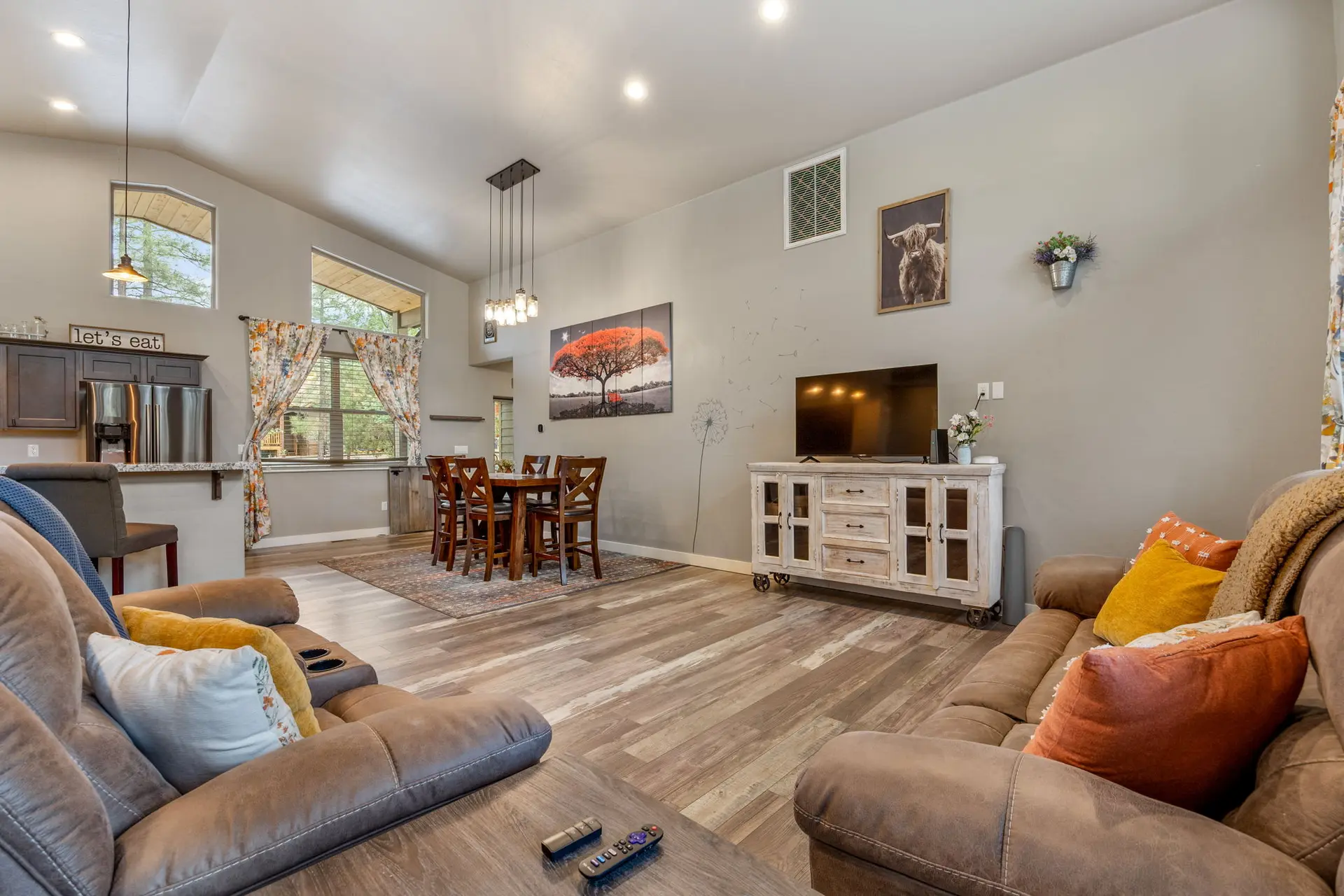A large living and dining area with brown couches, dining table, TV, and kitchen island.