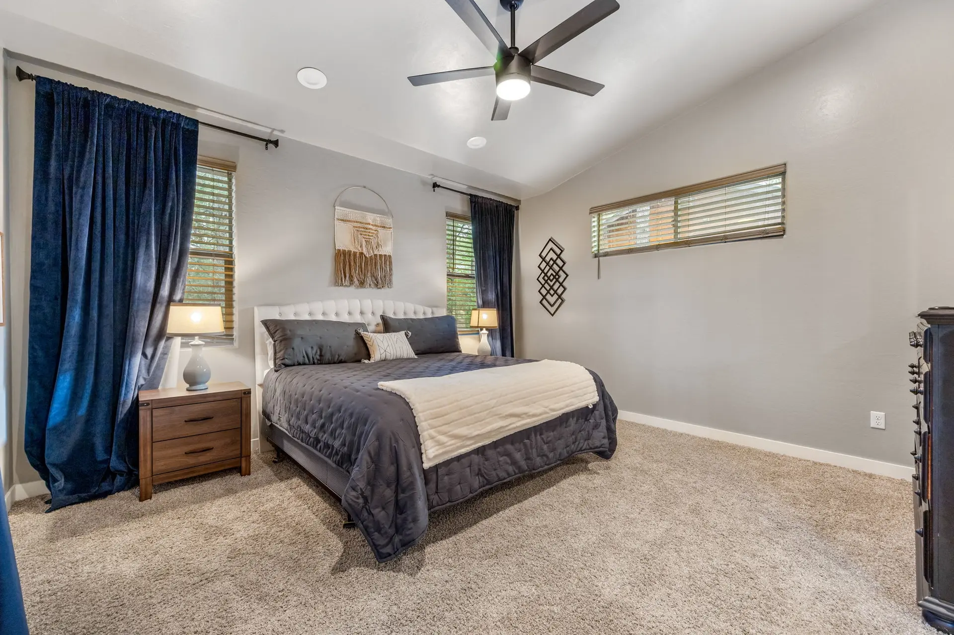 A spacious bedroom with a king-size bed, dark blue curtains, and a ceiling fan.