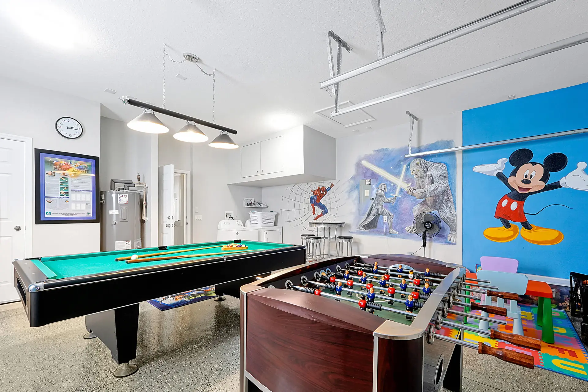 A pool table, foosball table, and Mickey Mouse mural in a game room.