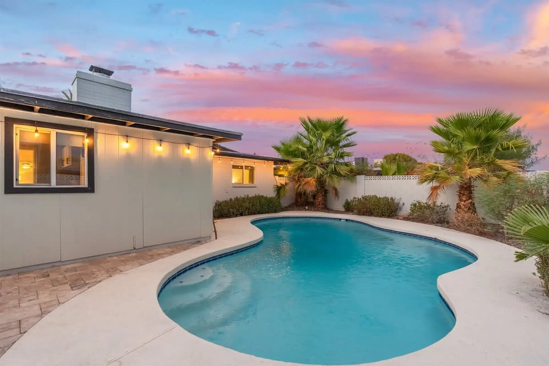 A house with a swimming pool and palm trees at sunset.