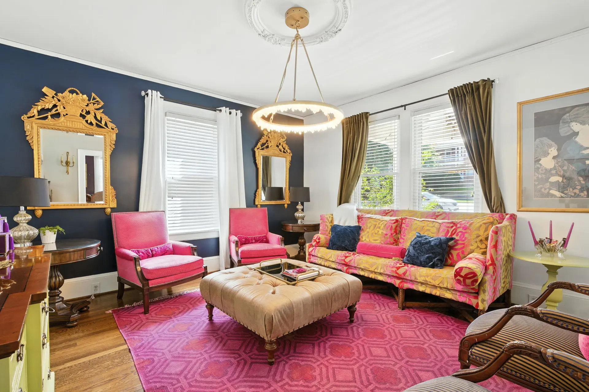 A vibrant living room with pink chairs, a colorful sofa, and a gold ornate mirror.