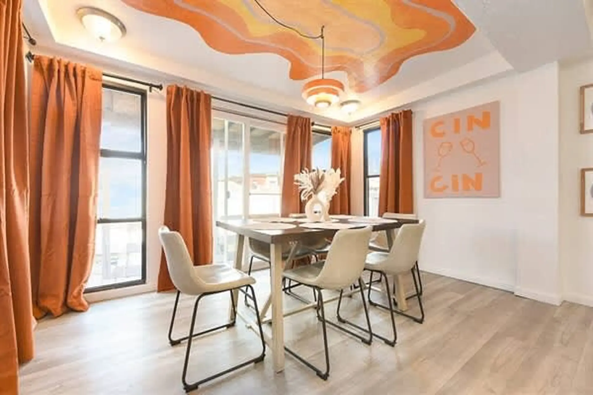 A dining room with a geometric ceiling design, orange curtains, and white chairs around a table.