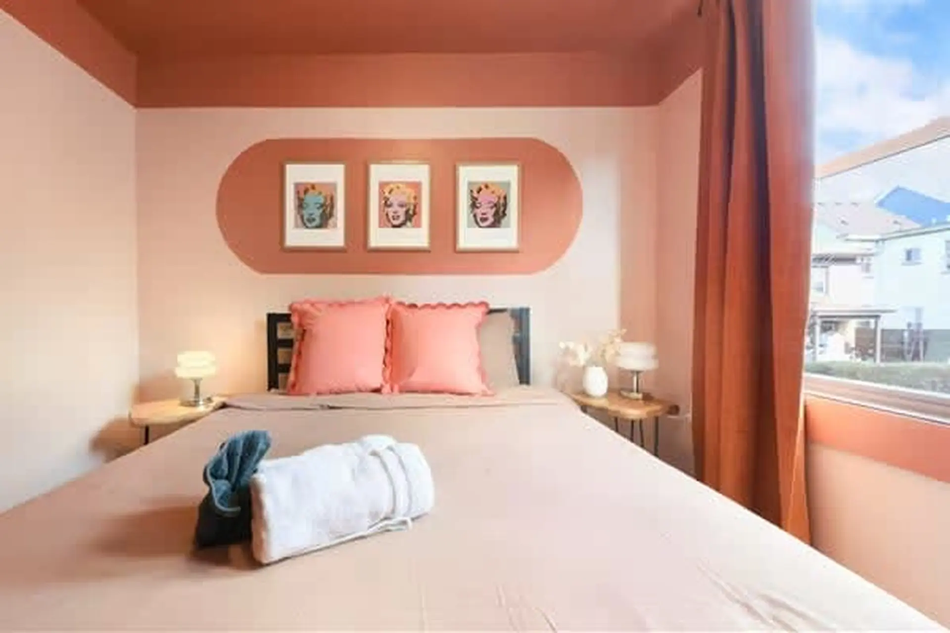 A bed with pink pillows and a bathrobe is in a room with a pink and orange theme.