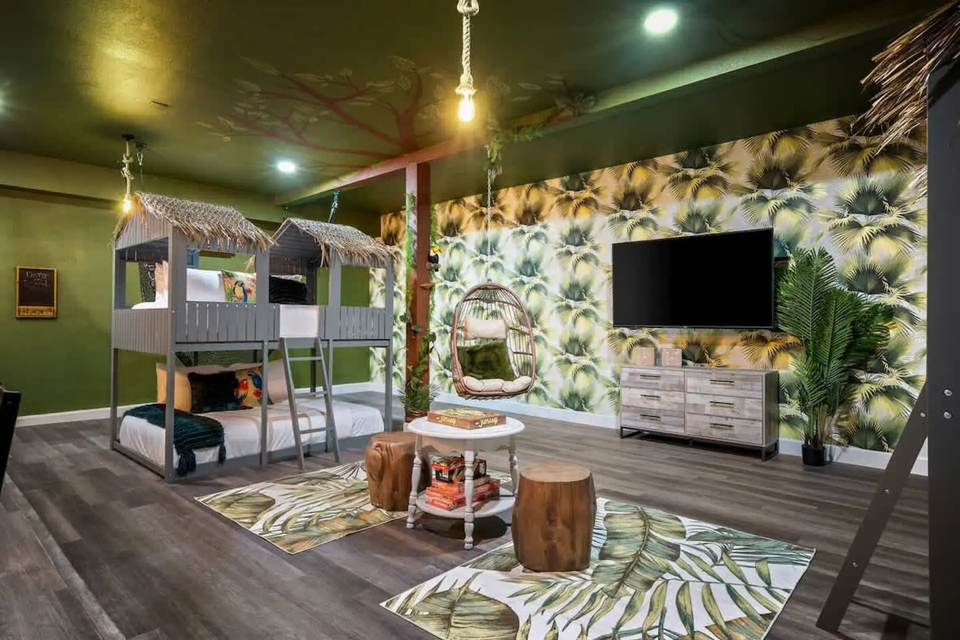 Kids' jungle-themed bedroom with bunk beds, a hanging chair, and palm-print wallpaper.