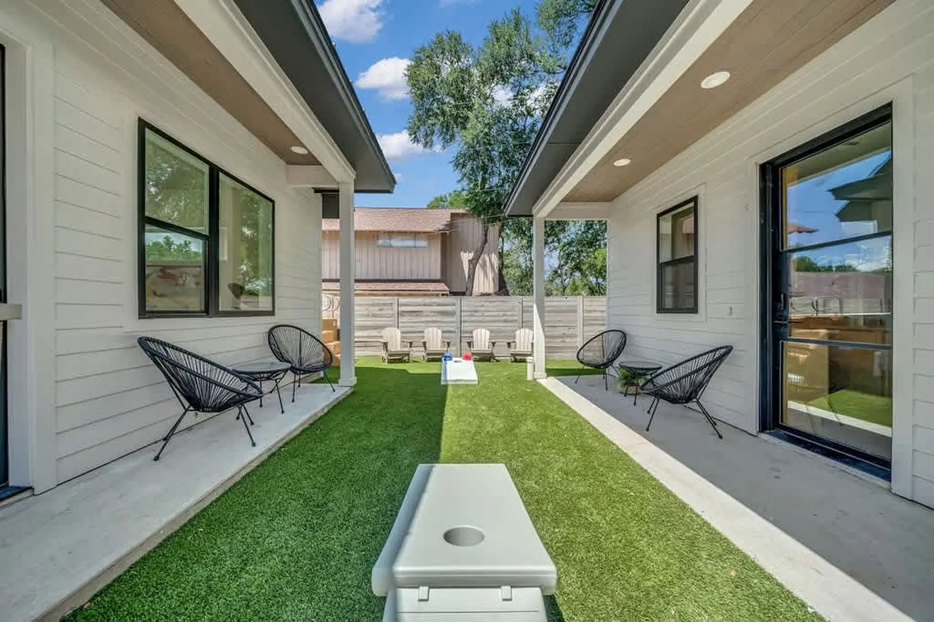 Modern backyard with artificial turf, chairs, and cornhole game.