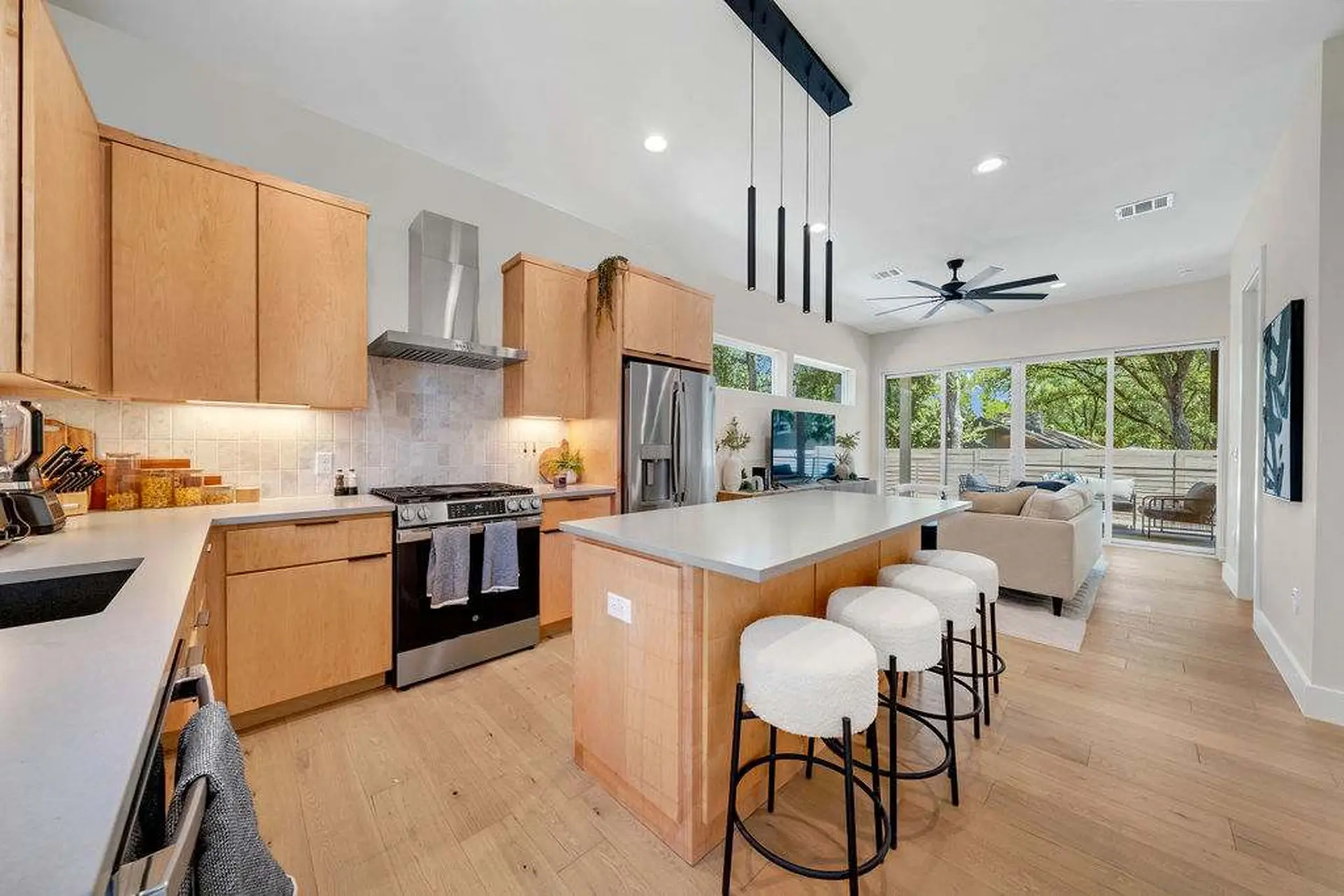 A bright kitchen with light wood cabinets, stainless steel appliances, and a large island with bar s