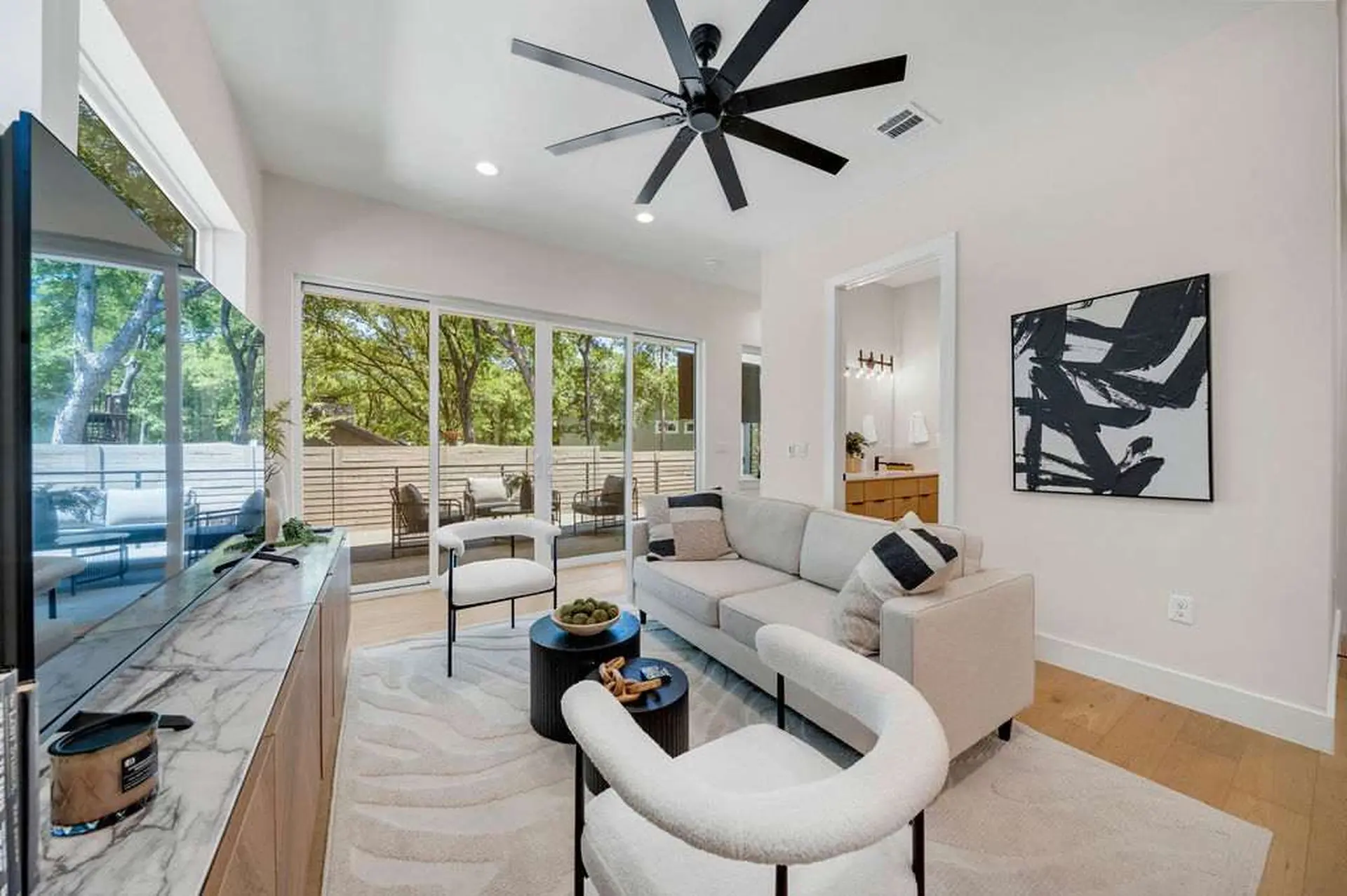 A living room with large sliding glass doors, a sectional sofa, and a black ceiling fan.