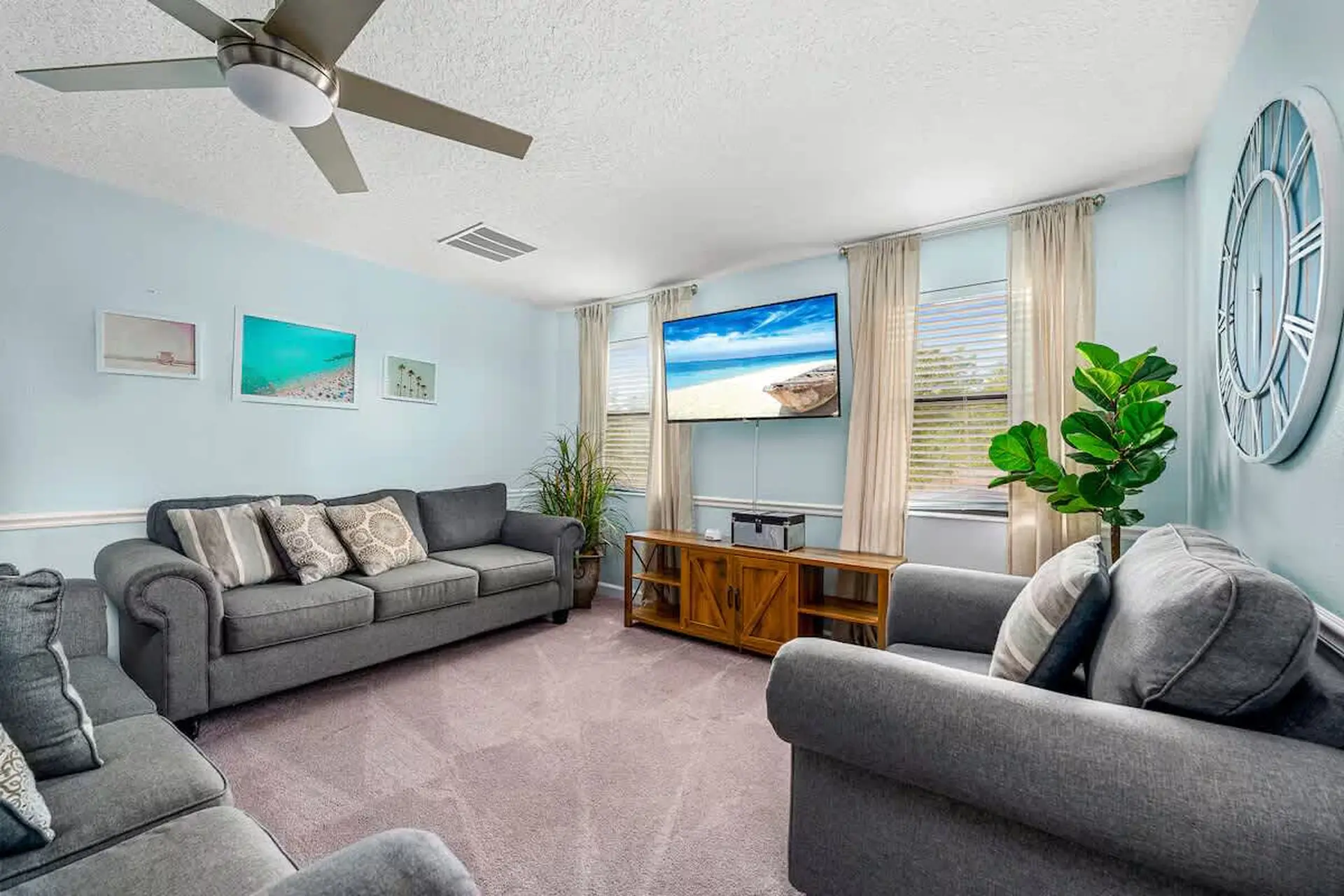A bright living room with a TV, sofas, and a ceiling fan.
