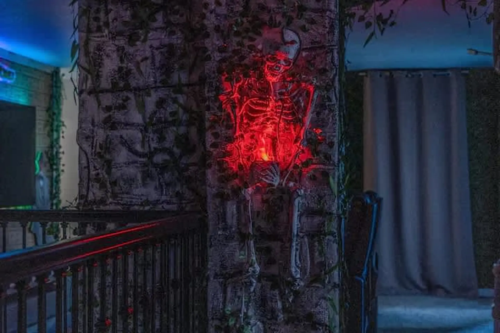 Creepy skeleton with red lights on a vine-covered stone pillar.