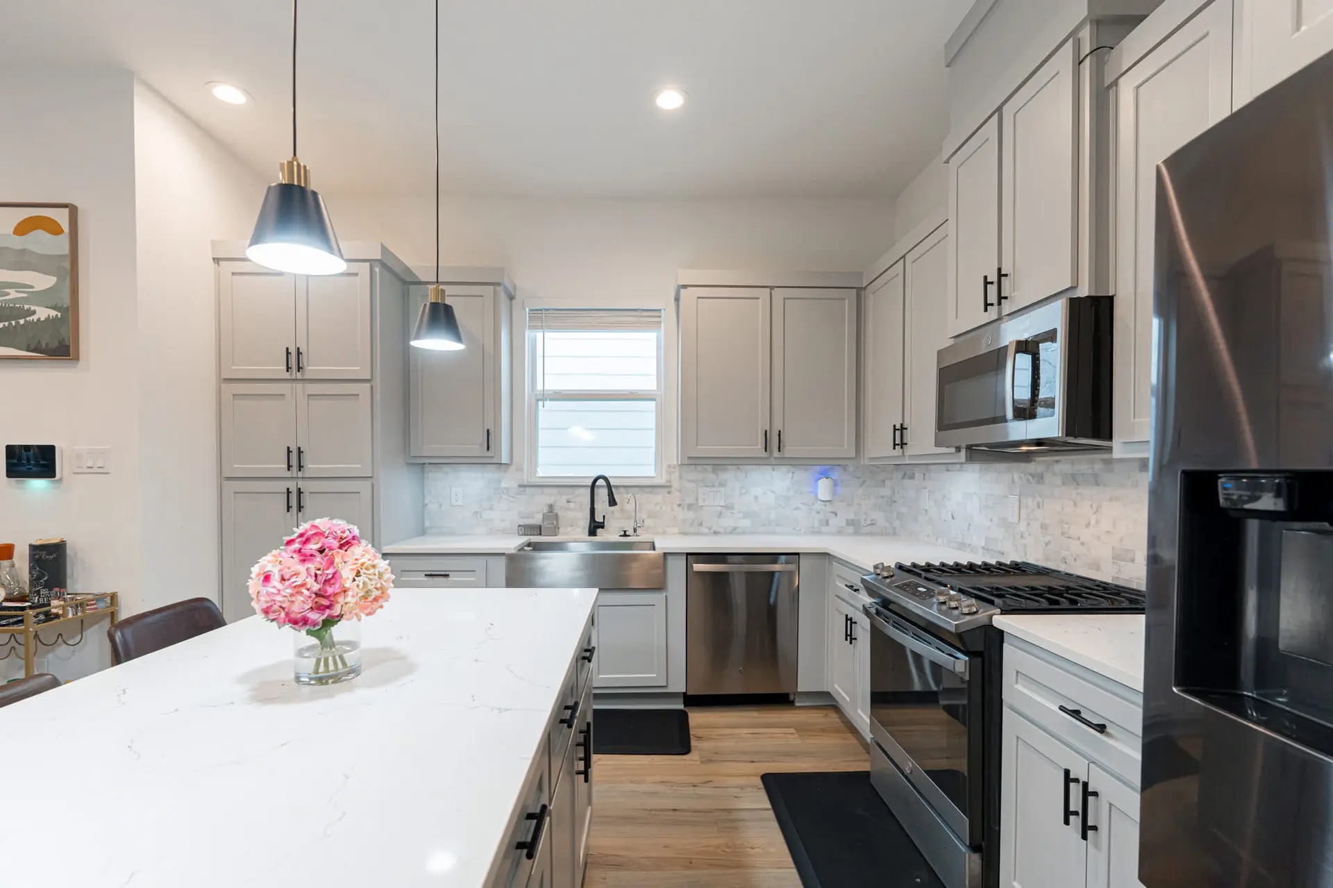 A modern kitchen with light gray cabinets, marble backsplash, and a stainless steel sink.