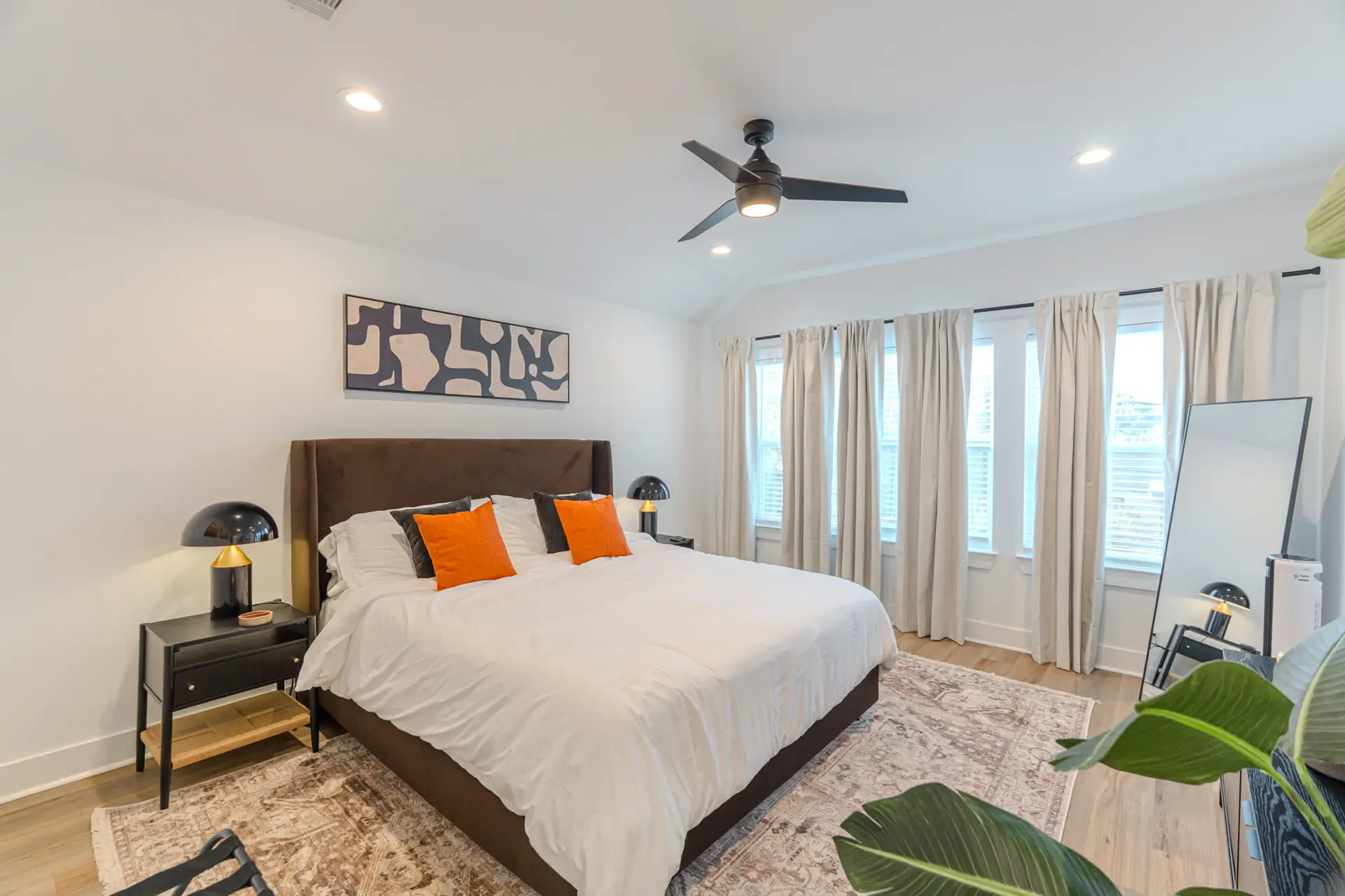 A modern bedroom with a dark brown bed, white bedding, and orange accent pillows.