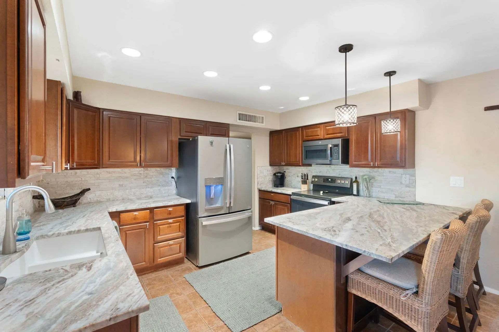 A bright kitchen with light granite countertops, cherry wood cabinets, stainless steel appliances, a