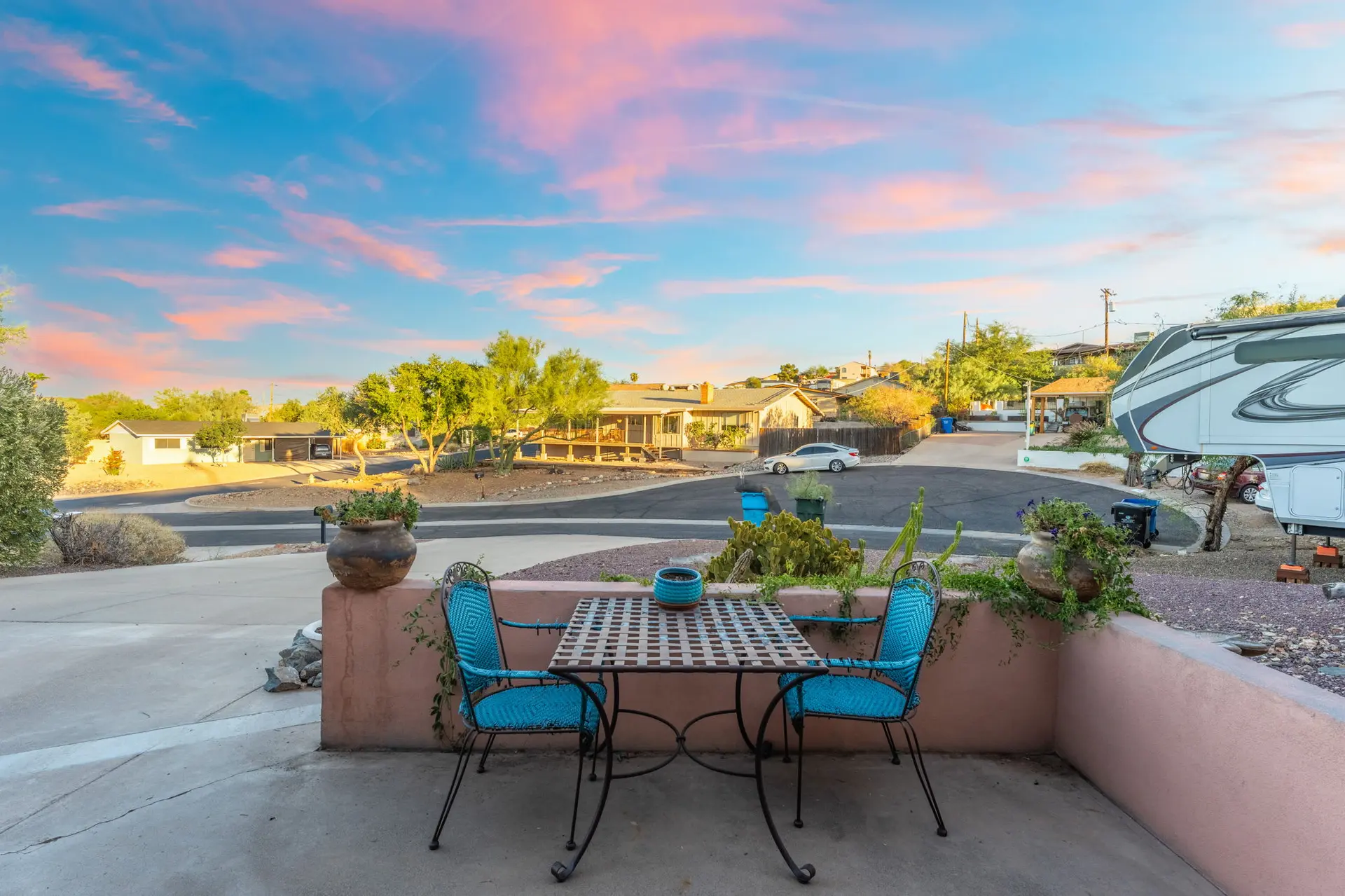 A patio table with two chairs sits on a concrete patio with a view of houses and a sunset sky.