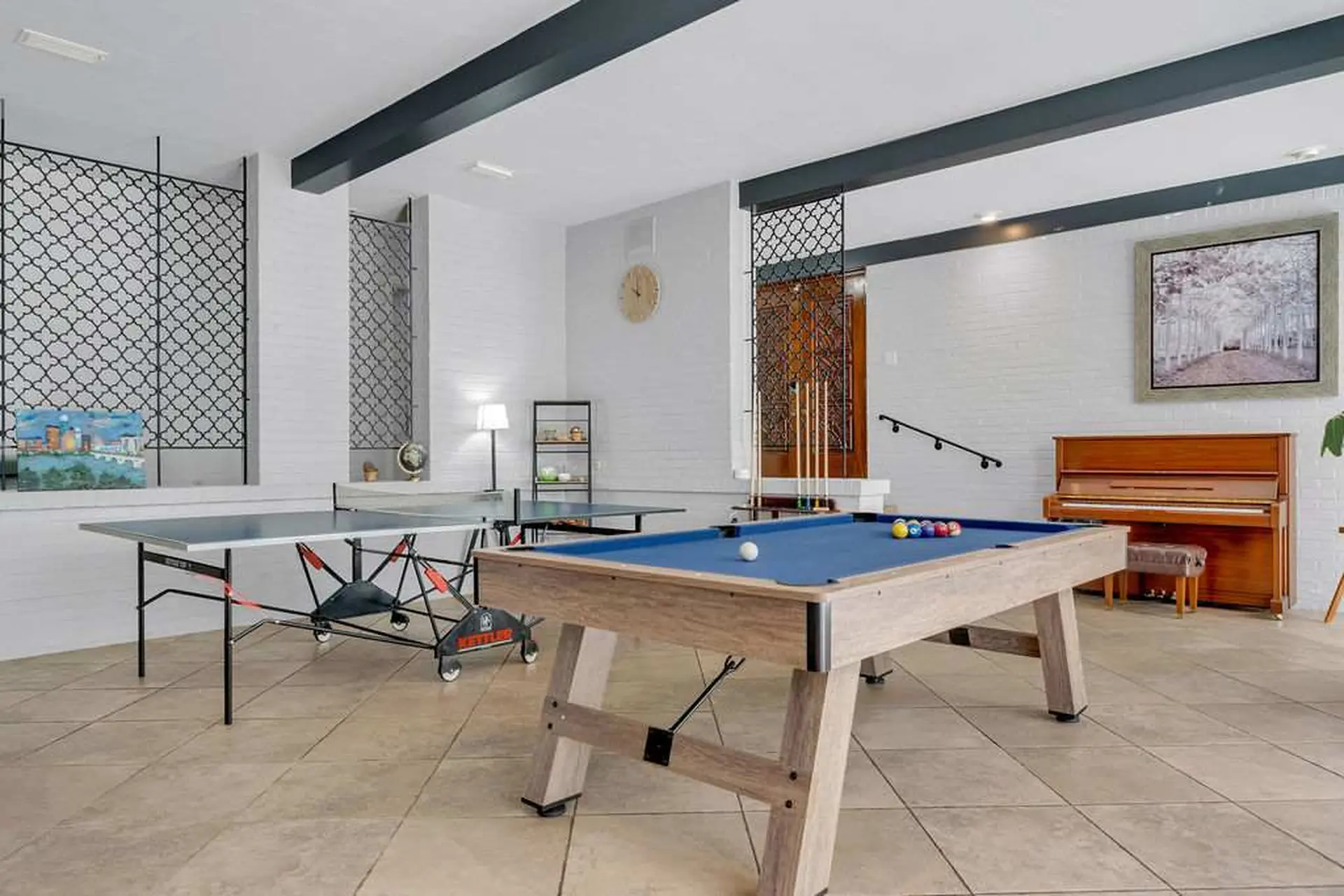 A pool table sits in front of a piano in a game room with ping pong tables.