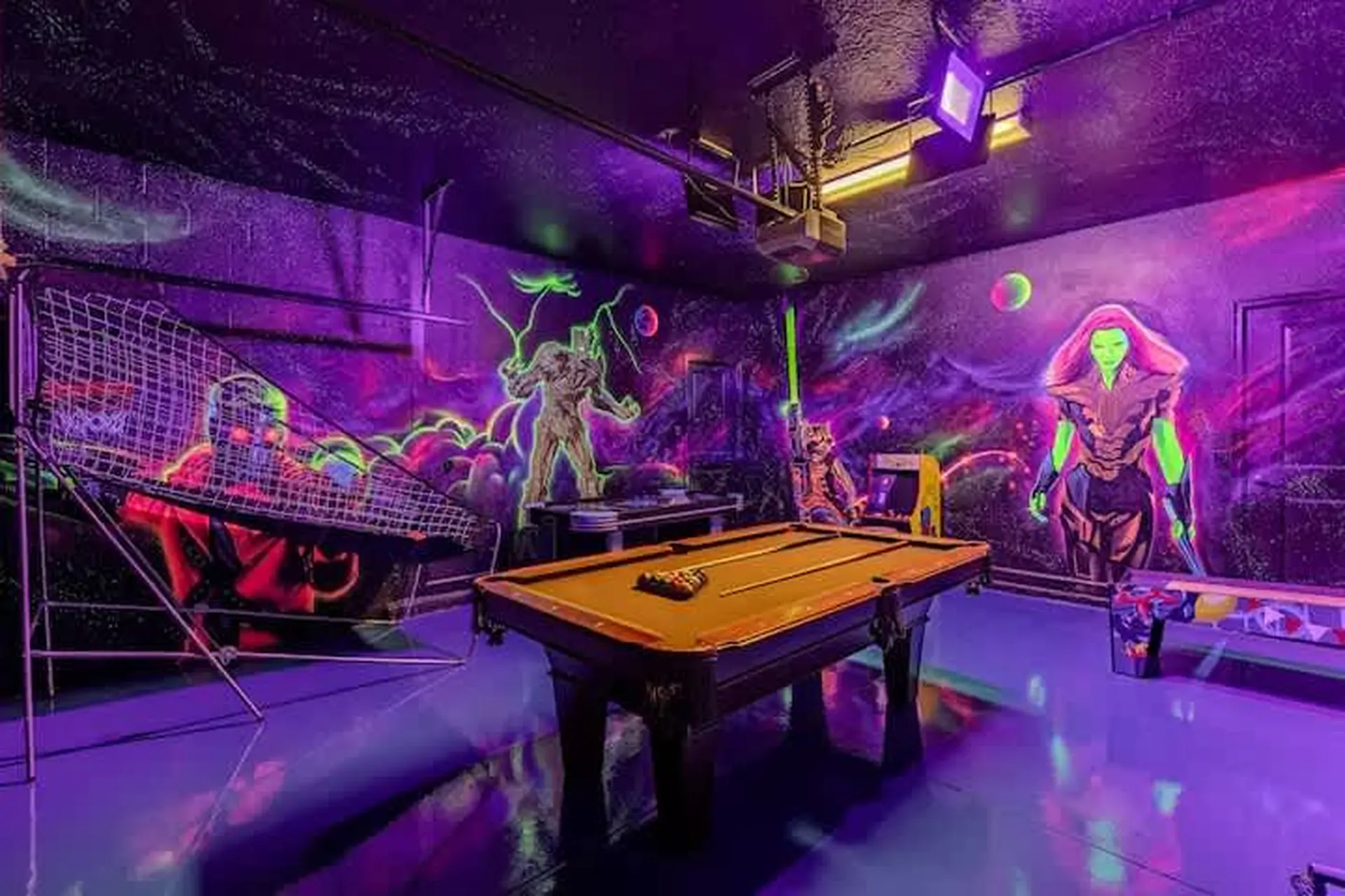 A neon-lit room with a pool table, arcade games, and graffiti art.
