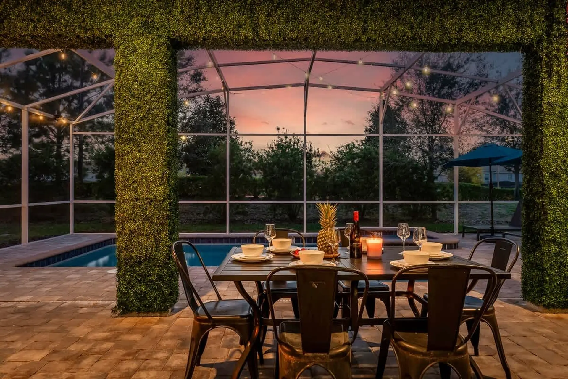 Outdoor dining area by pool at dusk with pineapple, wine, and lit candle.