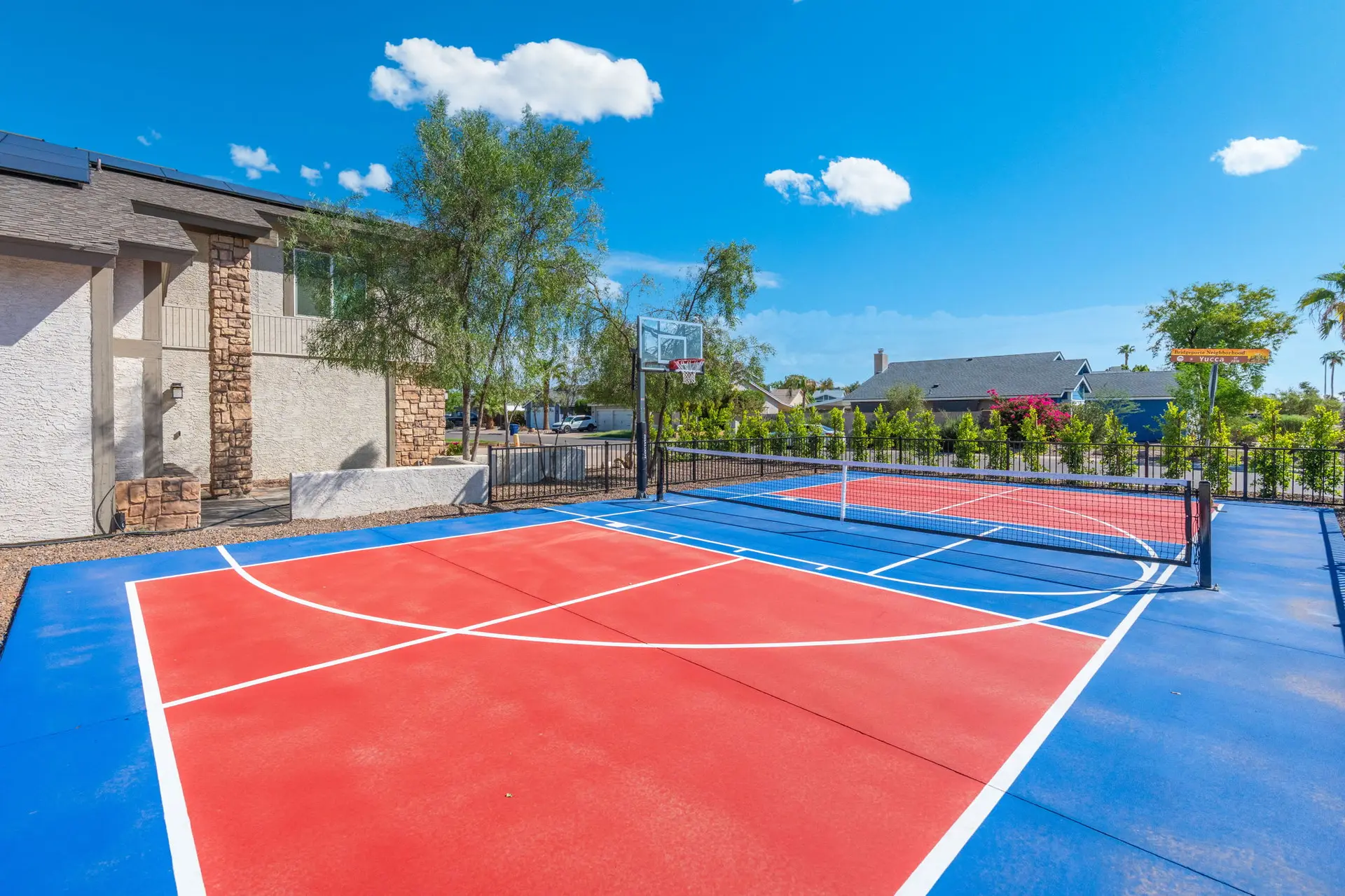 A bright blue and red multi-sport court with a basketball hoop and net under a clear blue sky.