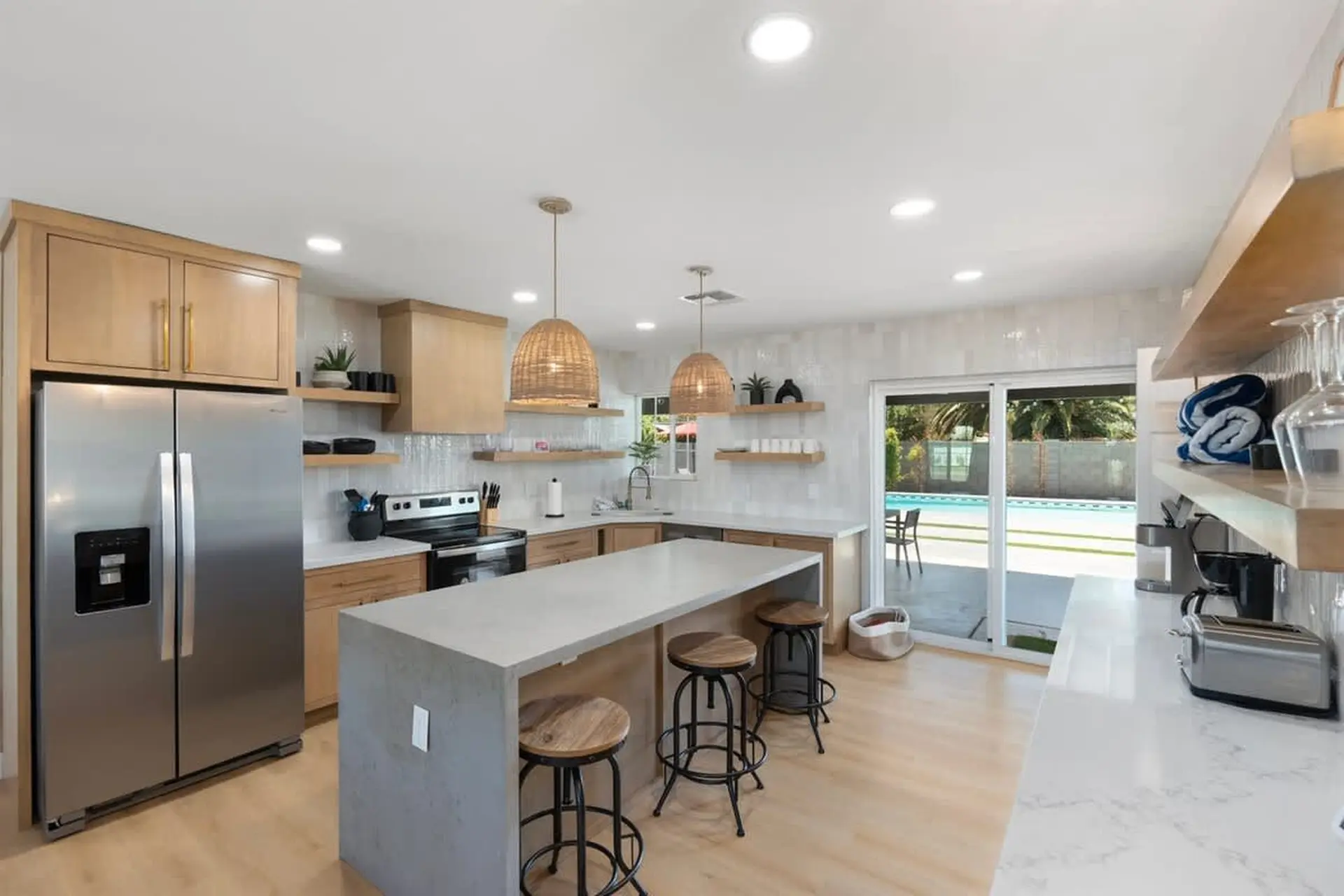 A modern kitchen with a large island, stainless steel appliances, and a view of a pool.