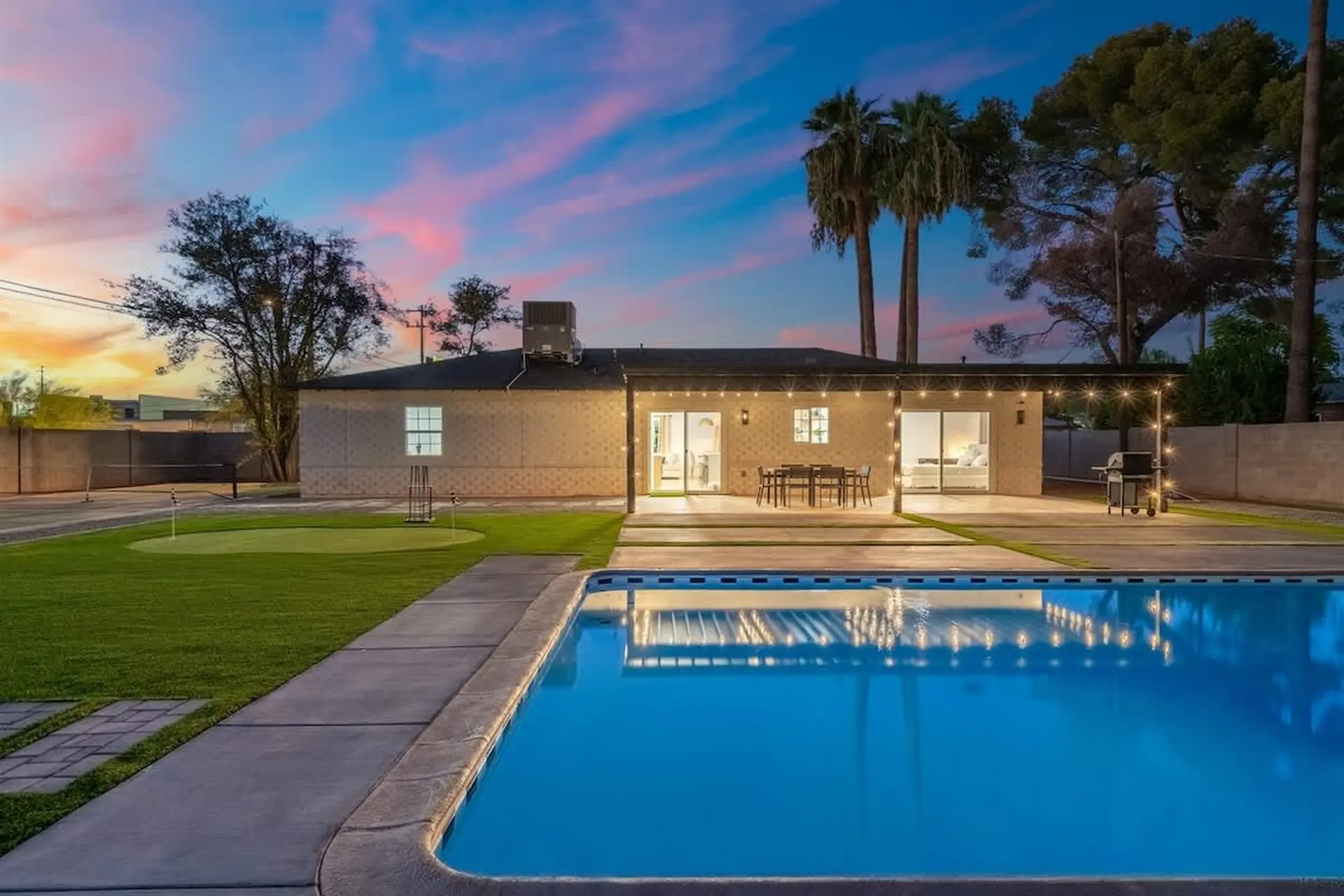 A backyard oasis featuring a swimming pool, putting green, and a patio with outdoor dining.