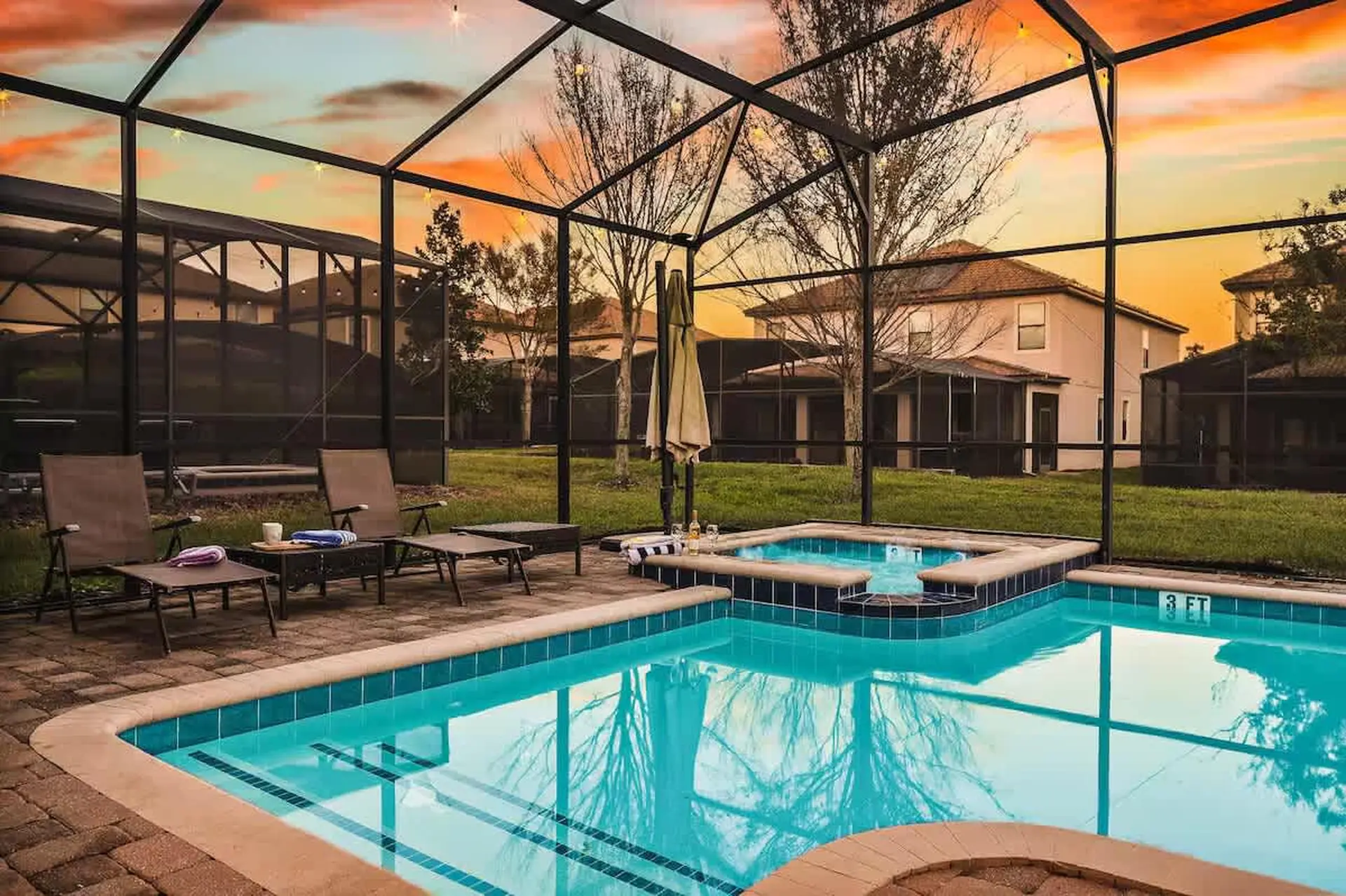 Screened-in patio with pool and hot tub at sunset with colorful sky.