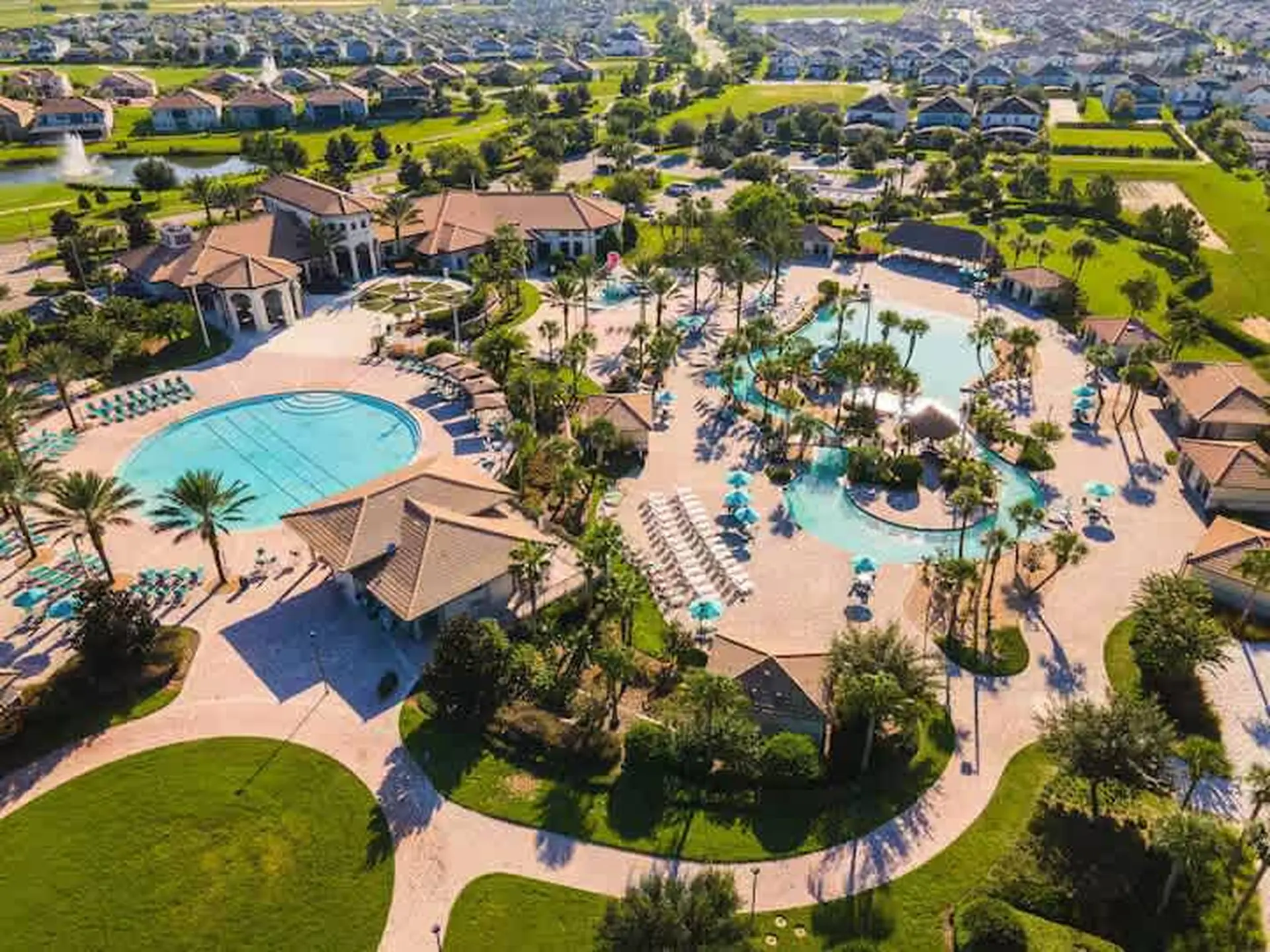 An aerial view of a resort with multiple pools, palm trees, and surrounding houses.