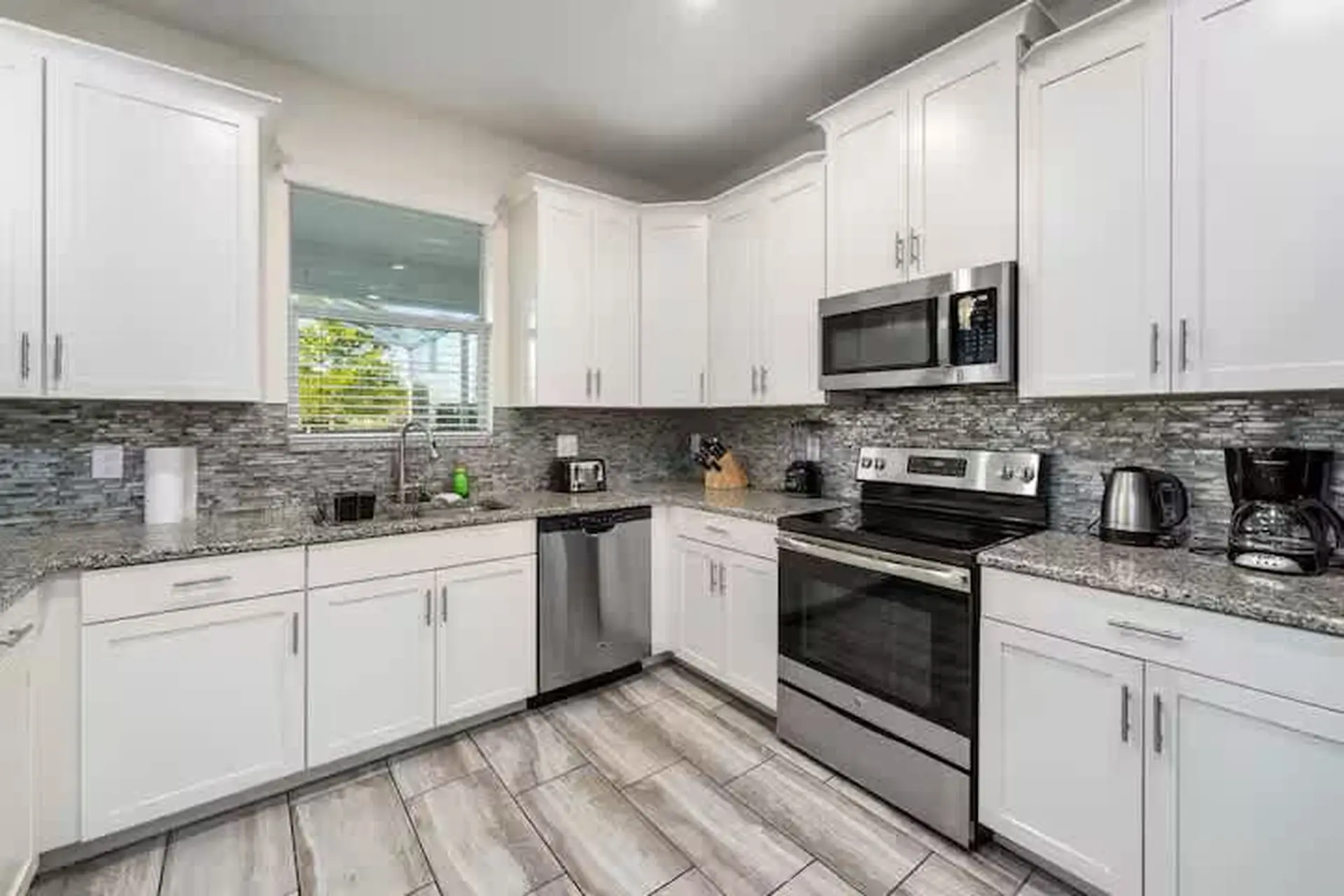 A clean kitchen with white cabinets, granite countertops, stainless steel appliances, and a subway t