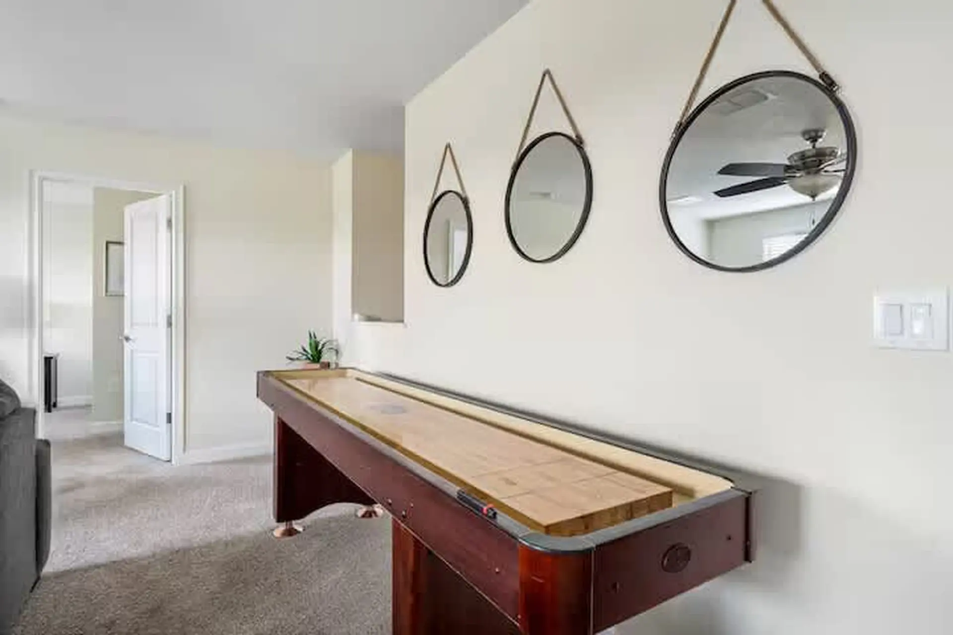 A shuffleboard table is in front of a white wall with three round mirrors hanging above it.