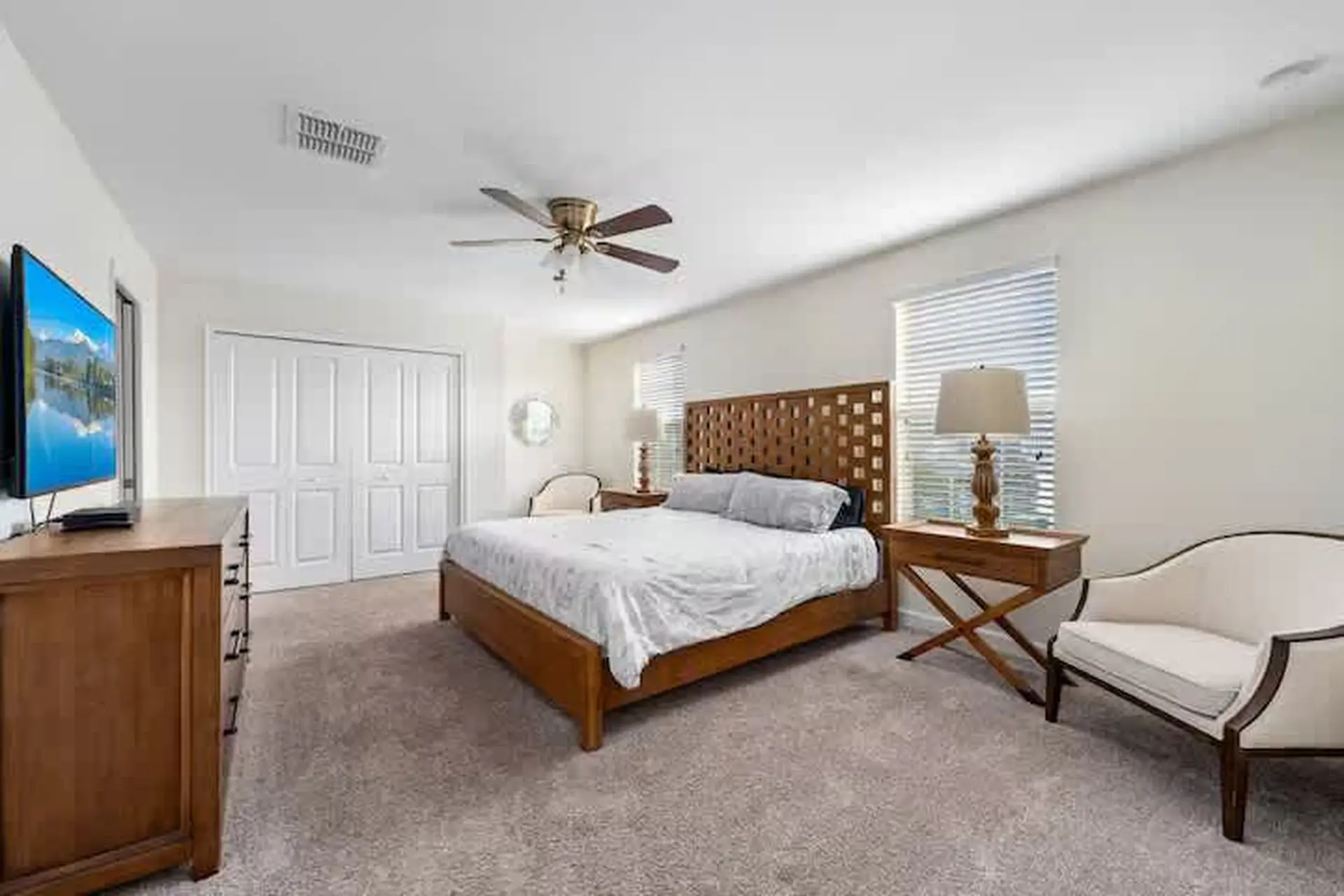 Bedroom with a king-size bed, dresser with TV, closet, chair, and side table with lamp.