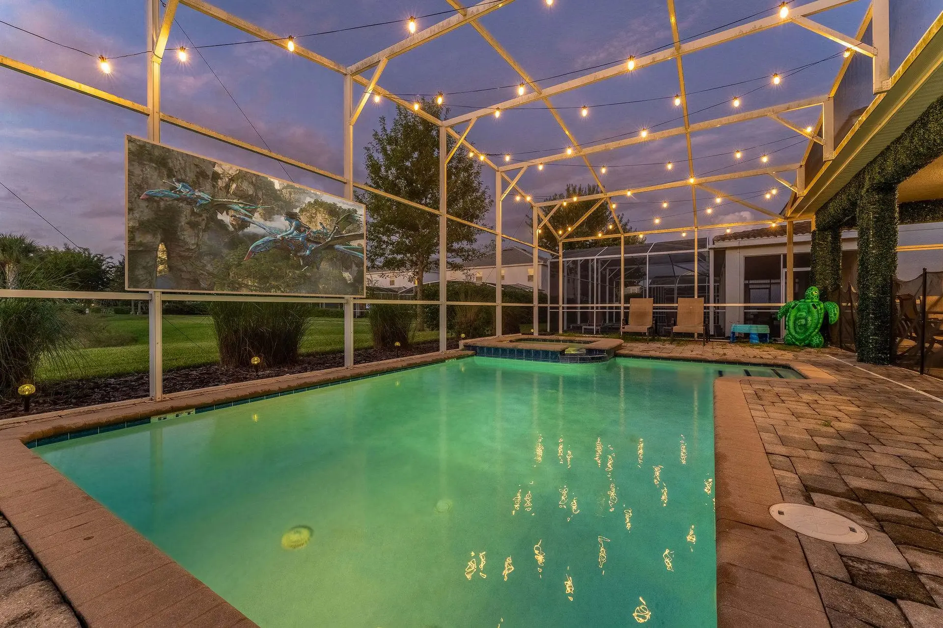 A screened-in pool area with string lights and a large screen displaying the movie Avatar.