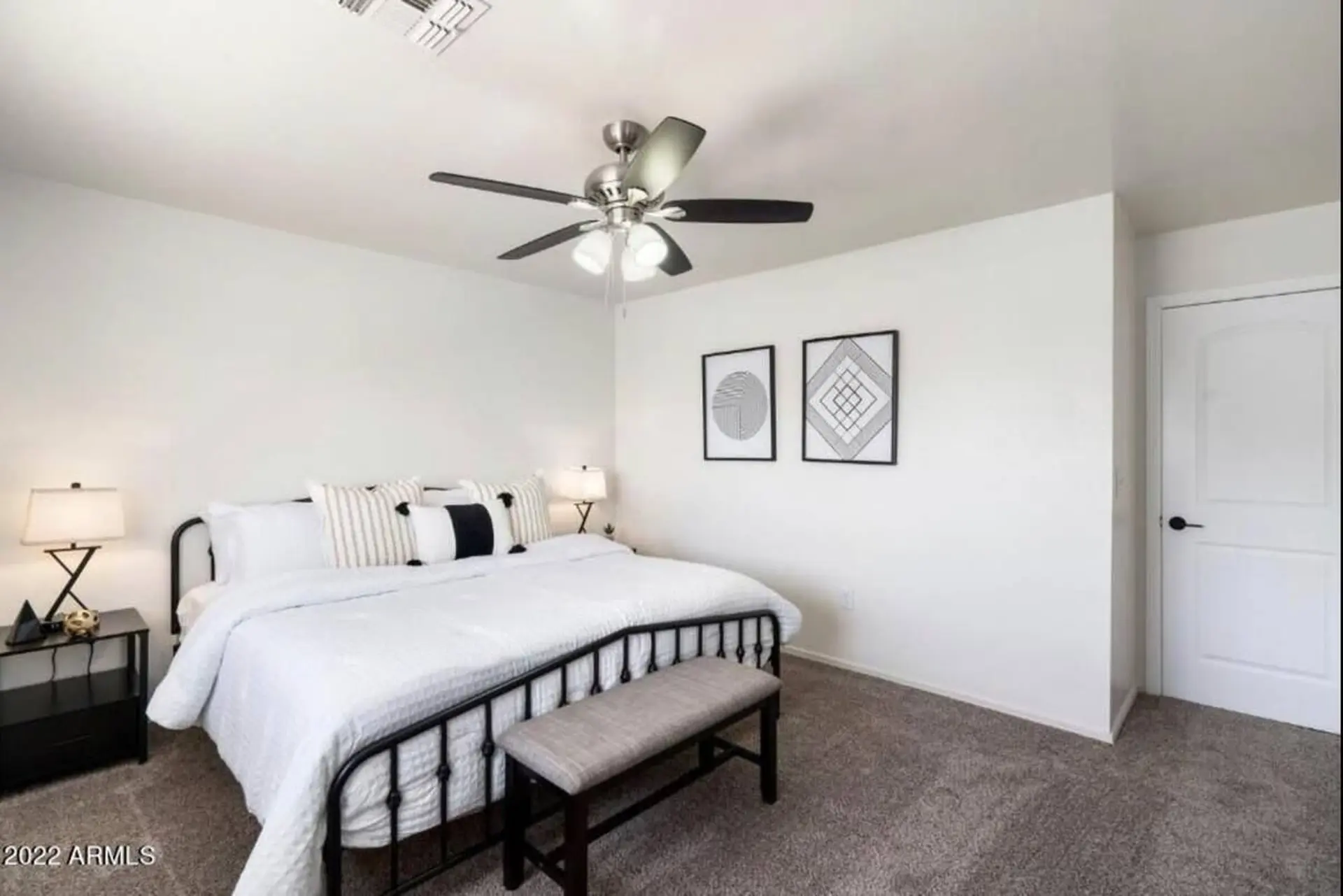 A minimalist bedroom with a black metal bed frame, white bedding, and modern art.