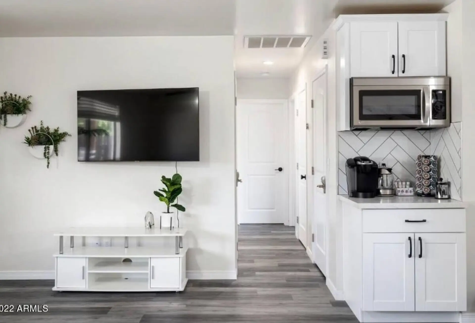 A modern living room with a TV, media console, and a kitchenette.