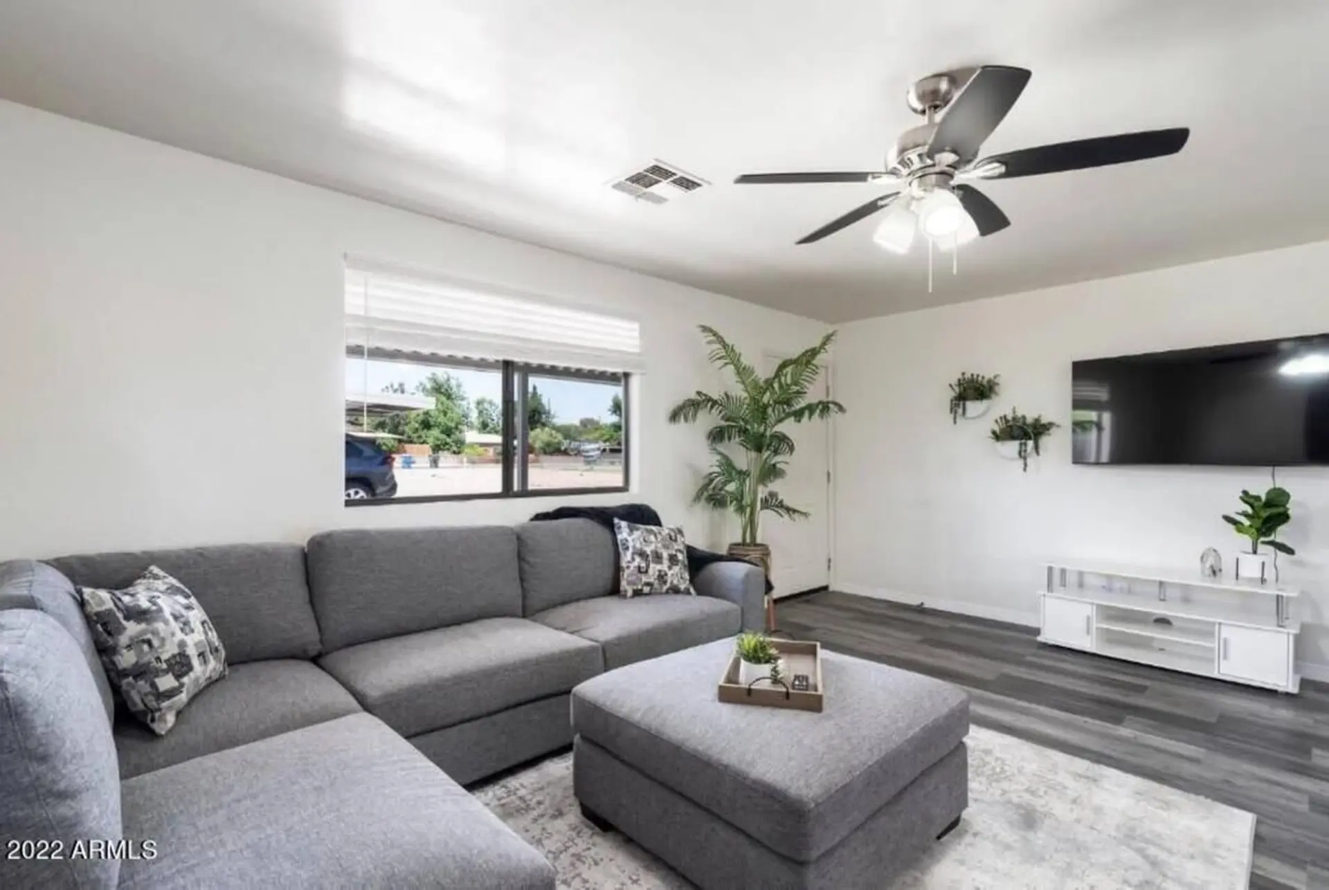 A modern living room with a gray sectional sofa, ottoman, and a large TV.