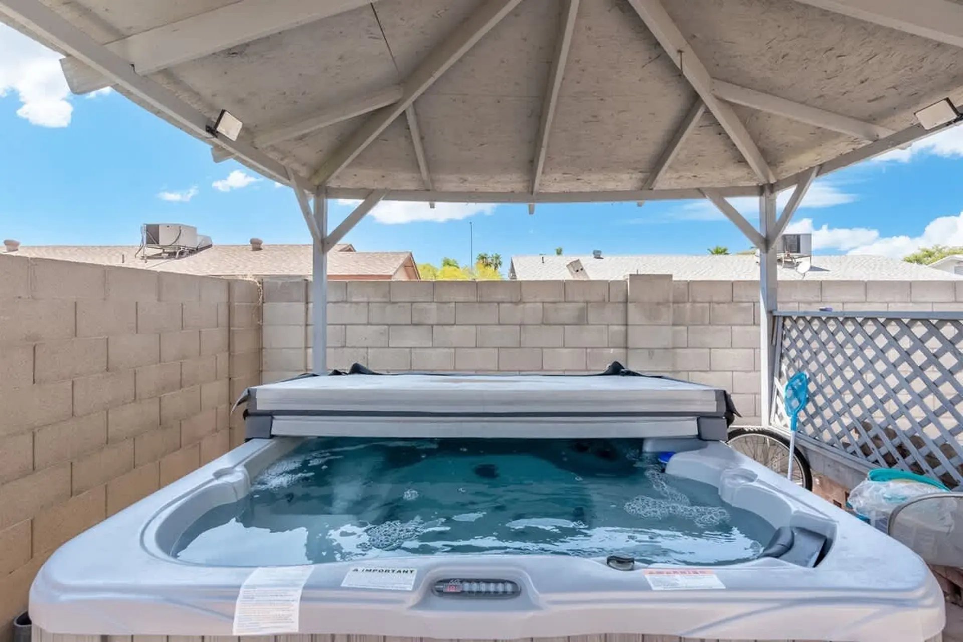 A hot tub is under a white gazebo with a tiled roof.