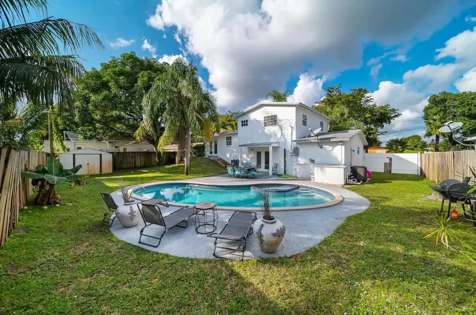 A backyard with a pool, lounge chairs, and a grill under a cloudy sky.