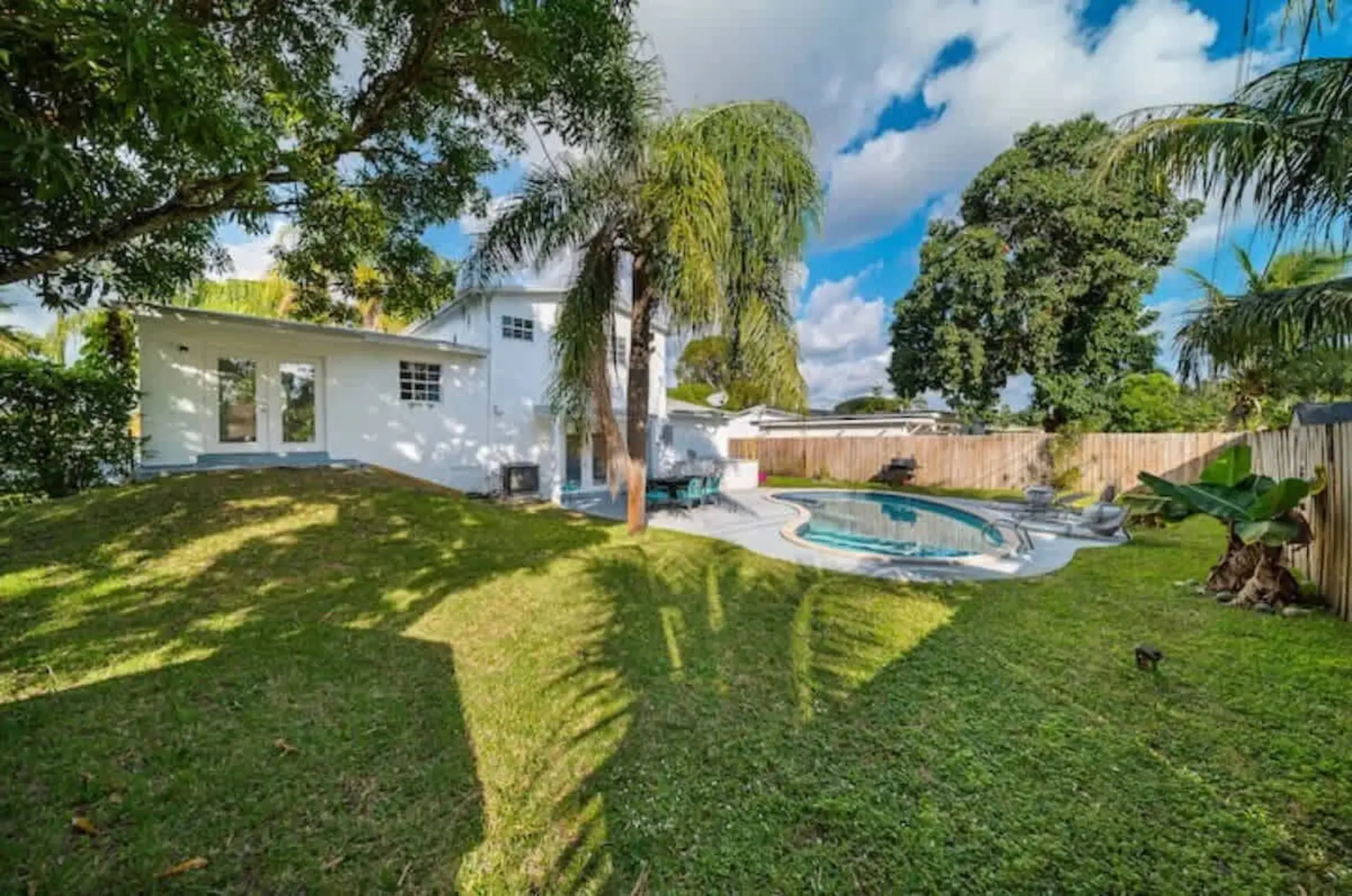 A white house with a pool and a lush green backyard on a sunny day.