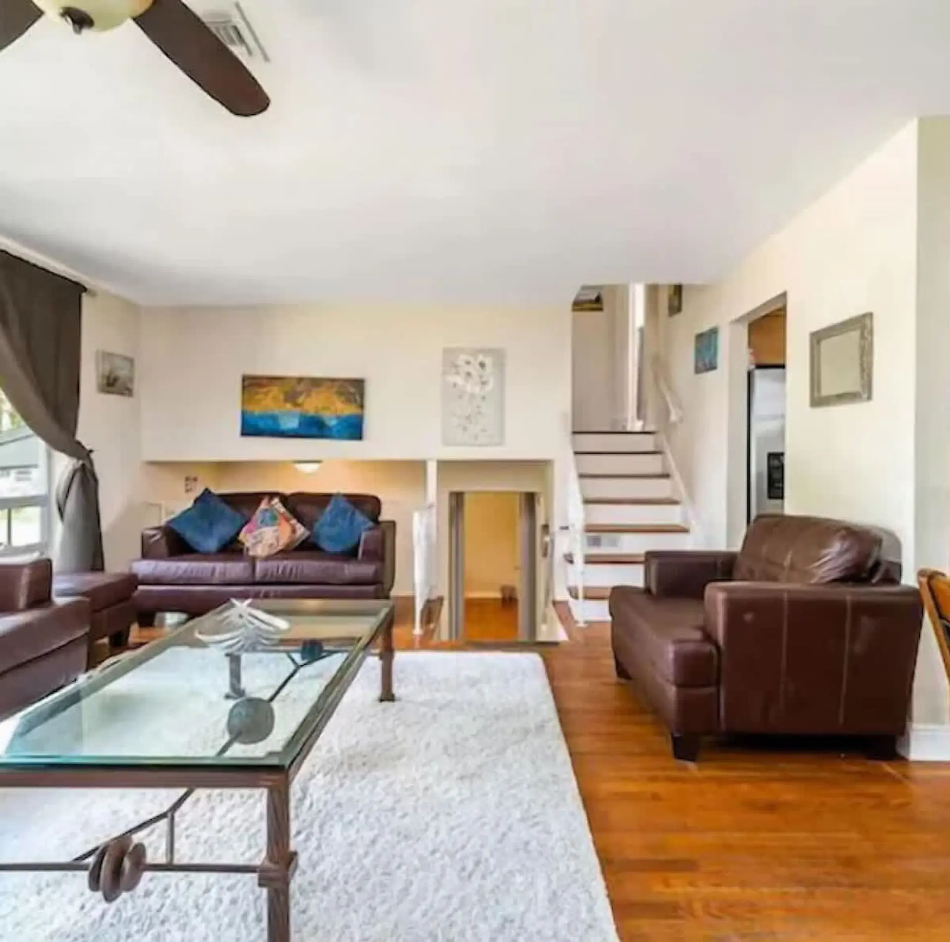 Living room with leather couches, glass coffee table, and stairs.
