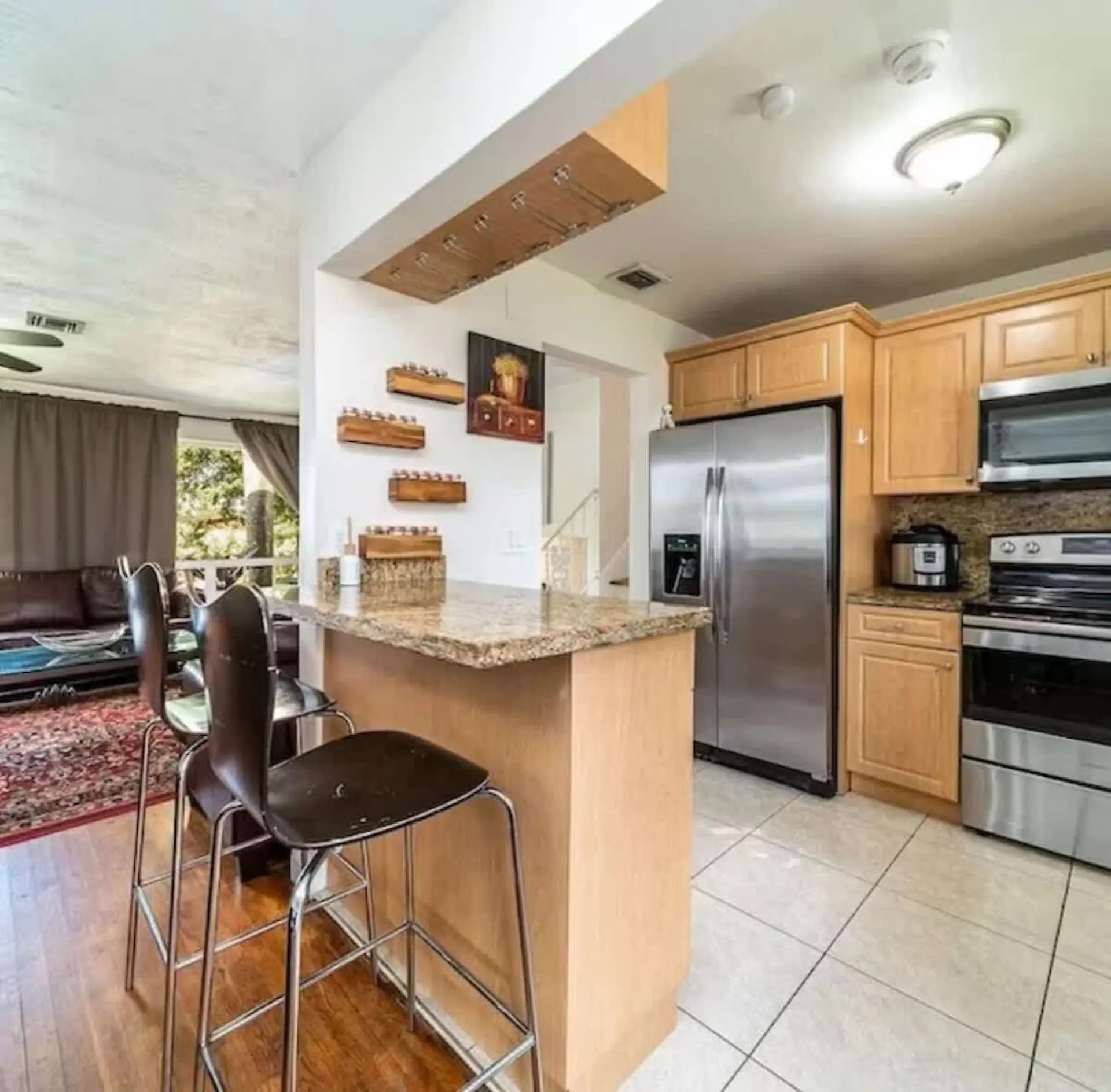 Kitchen island with bar stools and granite countertop, next to stainless steel appliances.