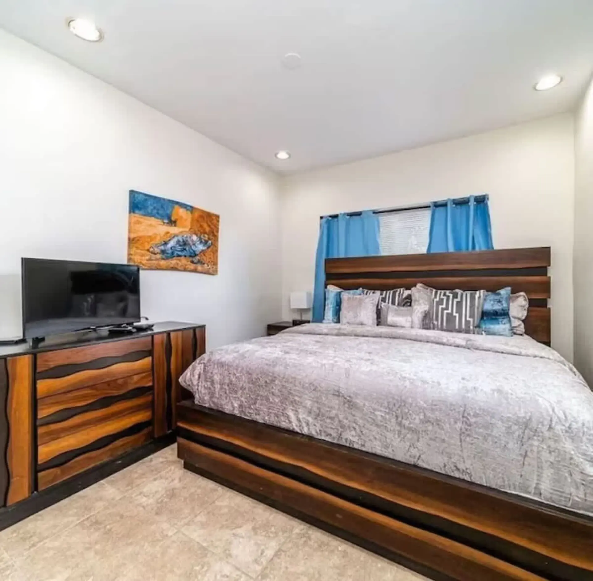 A bedroom with a large bed, a dresser with a TV, and blue curtains.