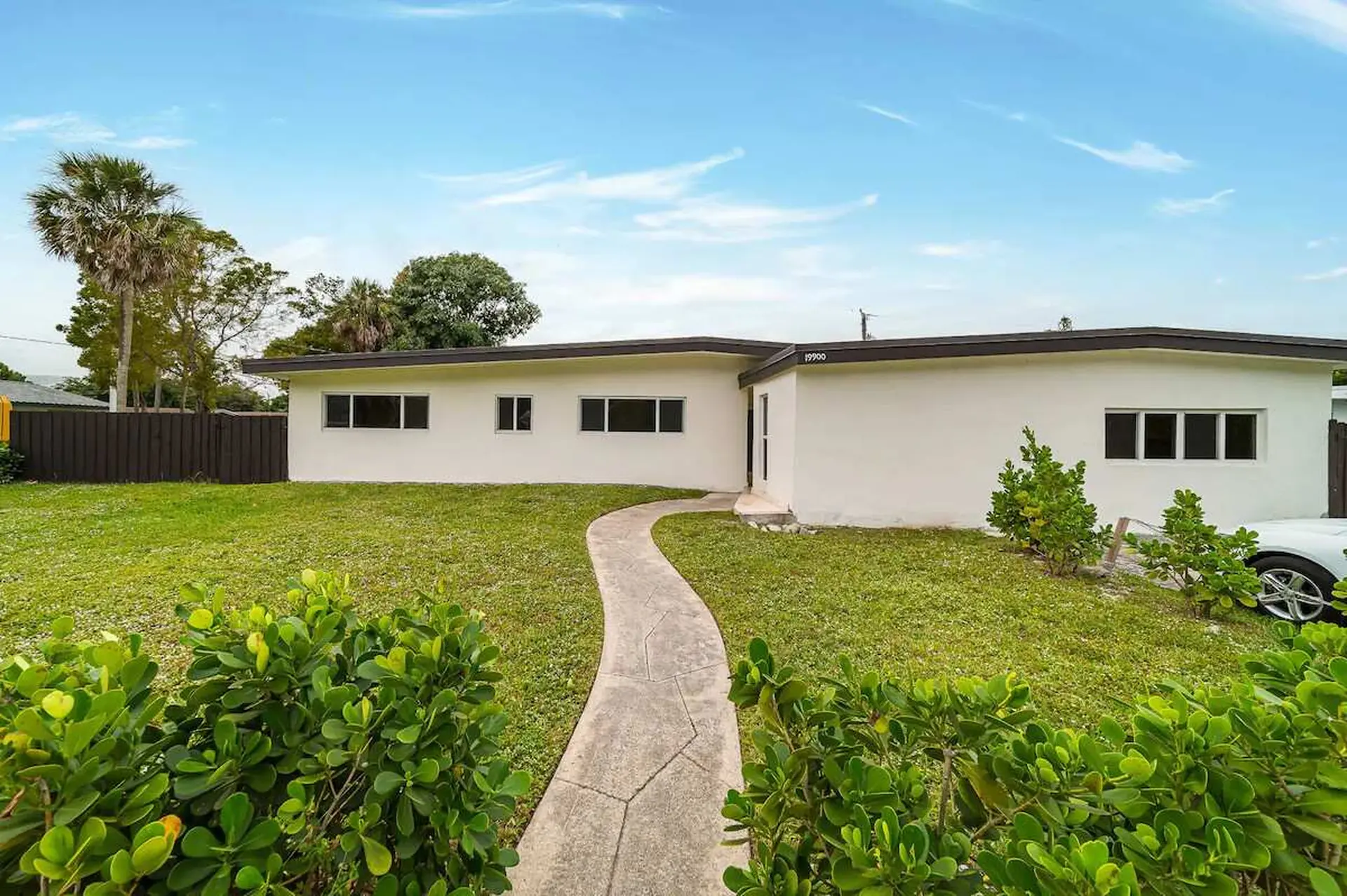 A stucco house with a dark roof and a concrete walkway on a sunny day.