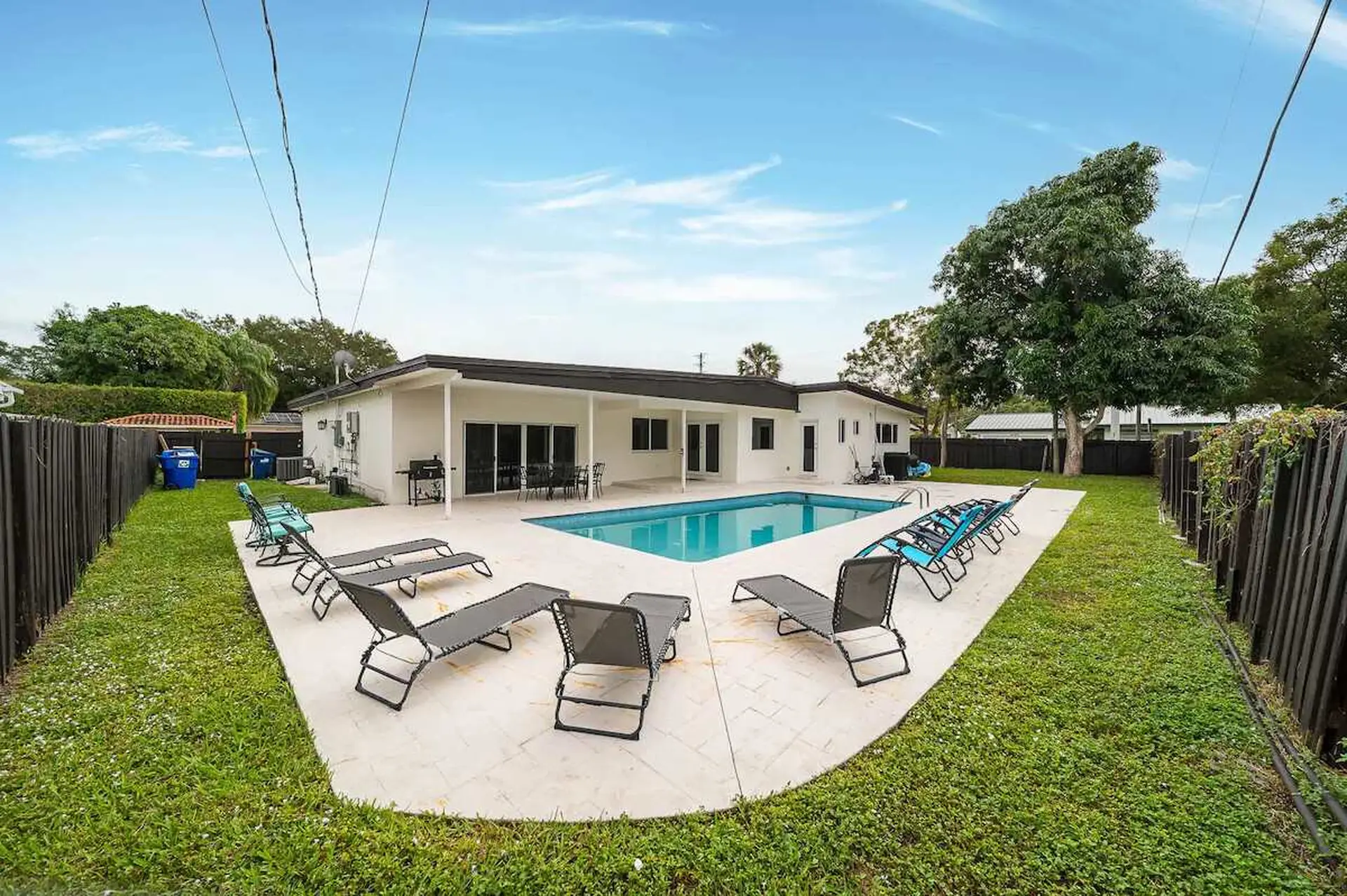 A backyard with a pool, lounge chairs, and a white house.