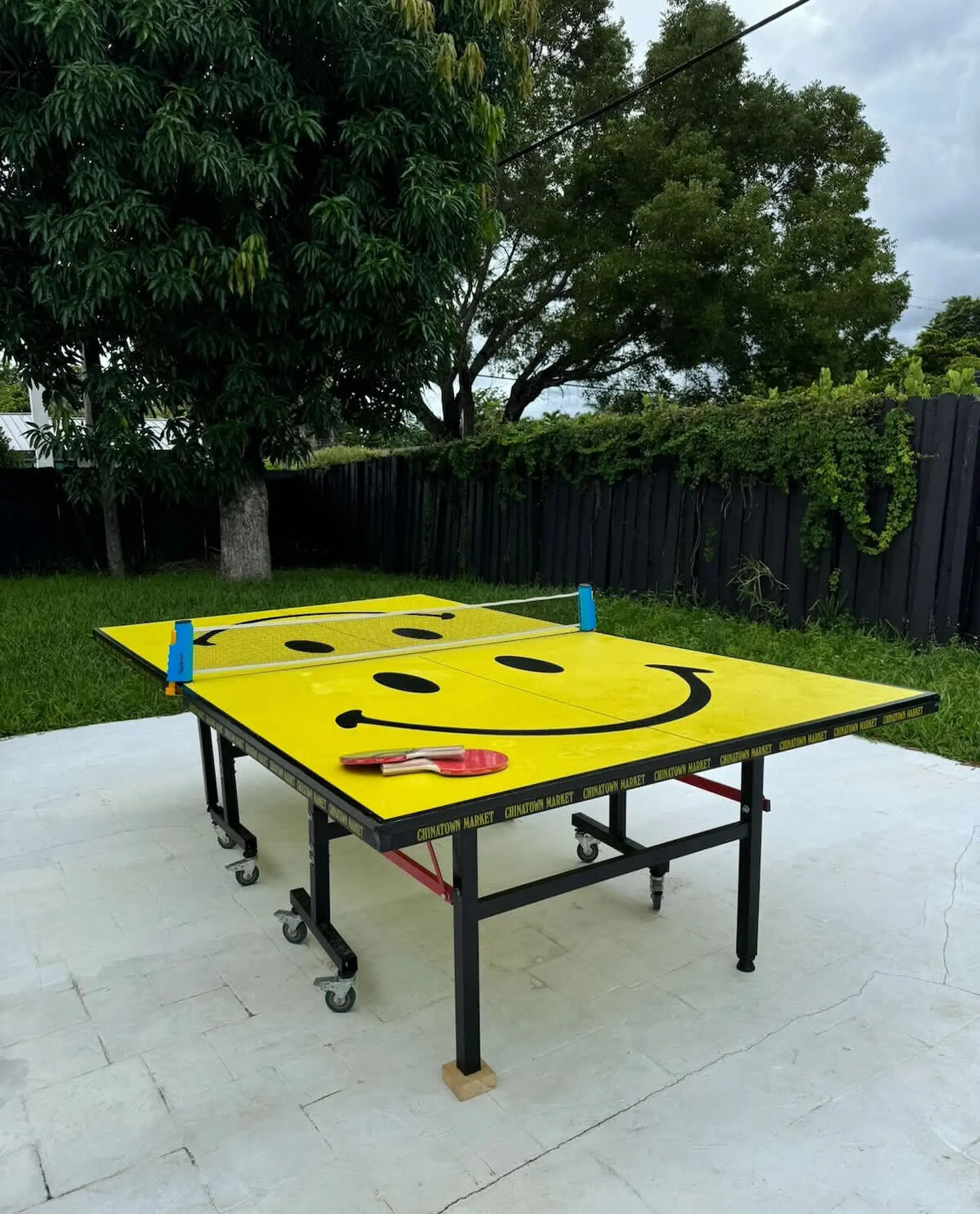 A yellow ping pong table with a smiley face design sits on a patio.