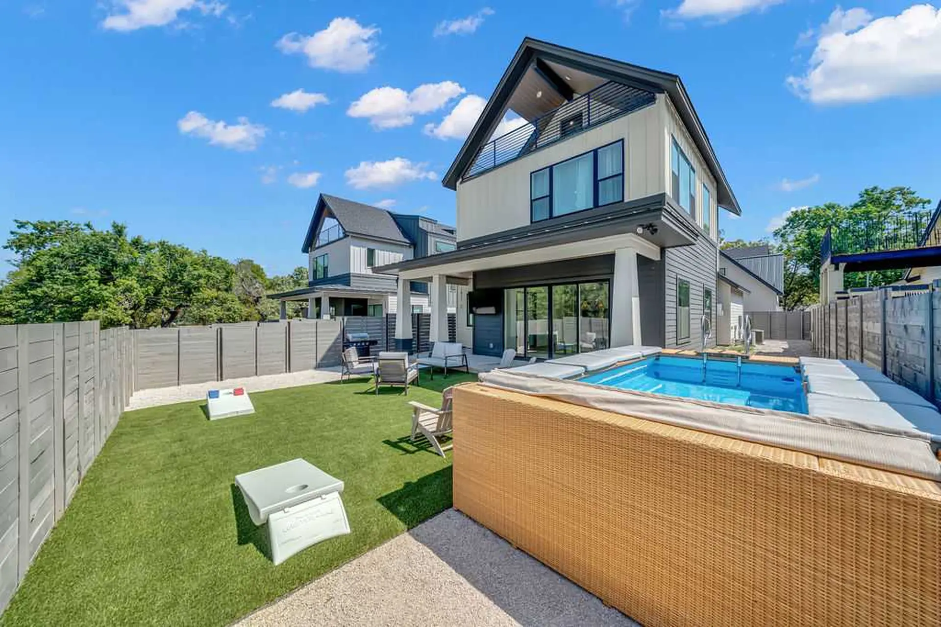 Modern backyard with a pool, patio furniture, and cornhole game.