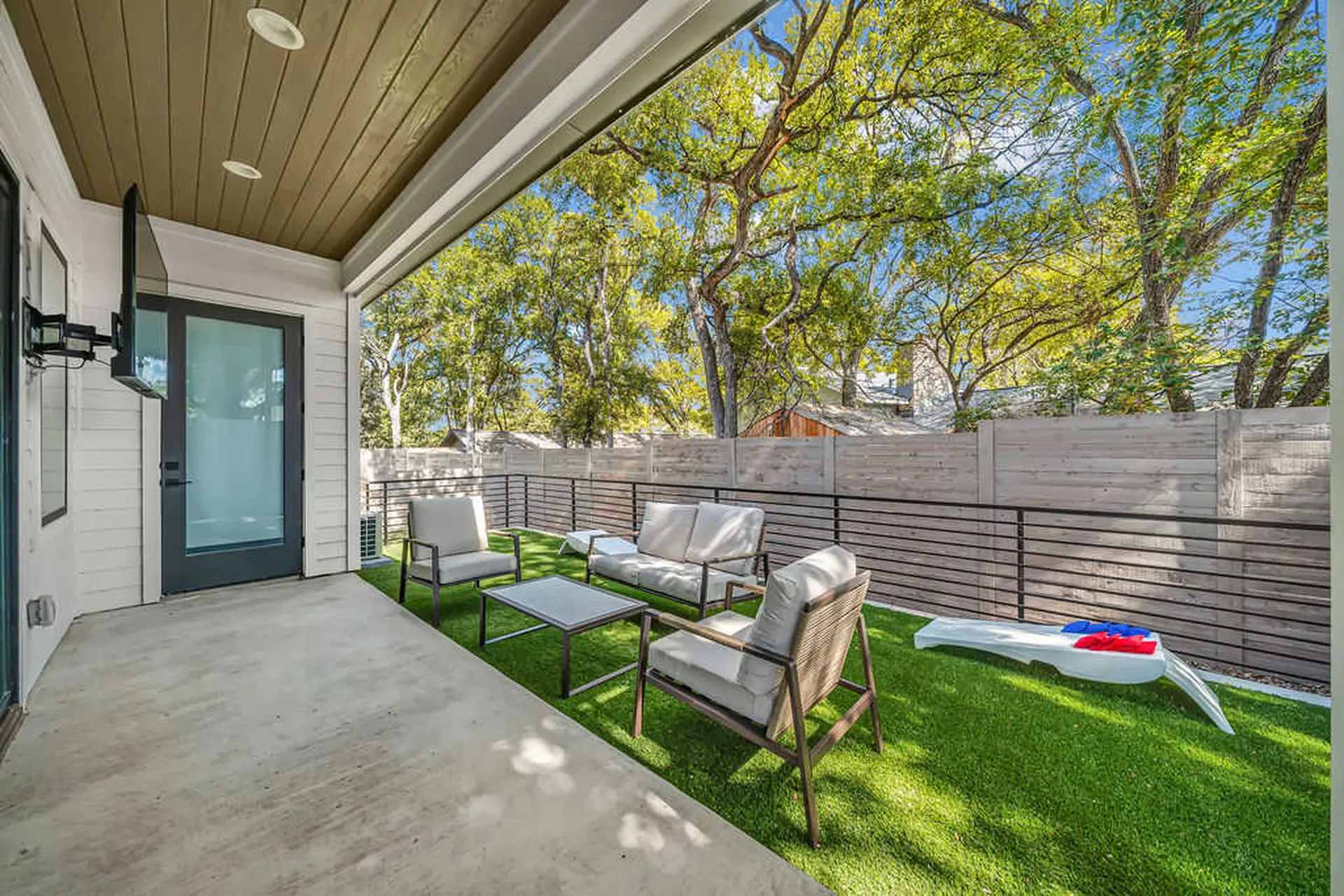 Covered patio with outdoor furniture and artificial grass in a backyard.