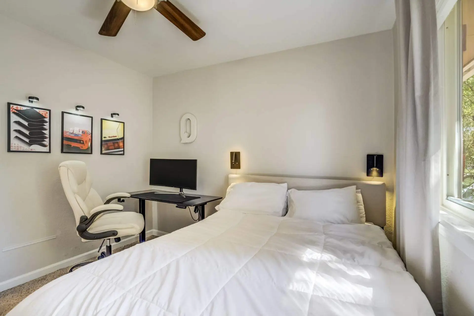 Modern bedroom with a white duvet, desk, chair, and artwork.