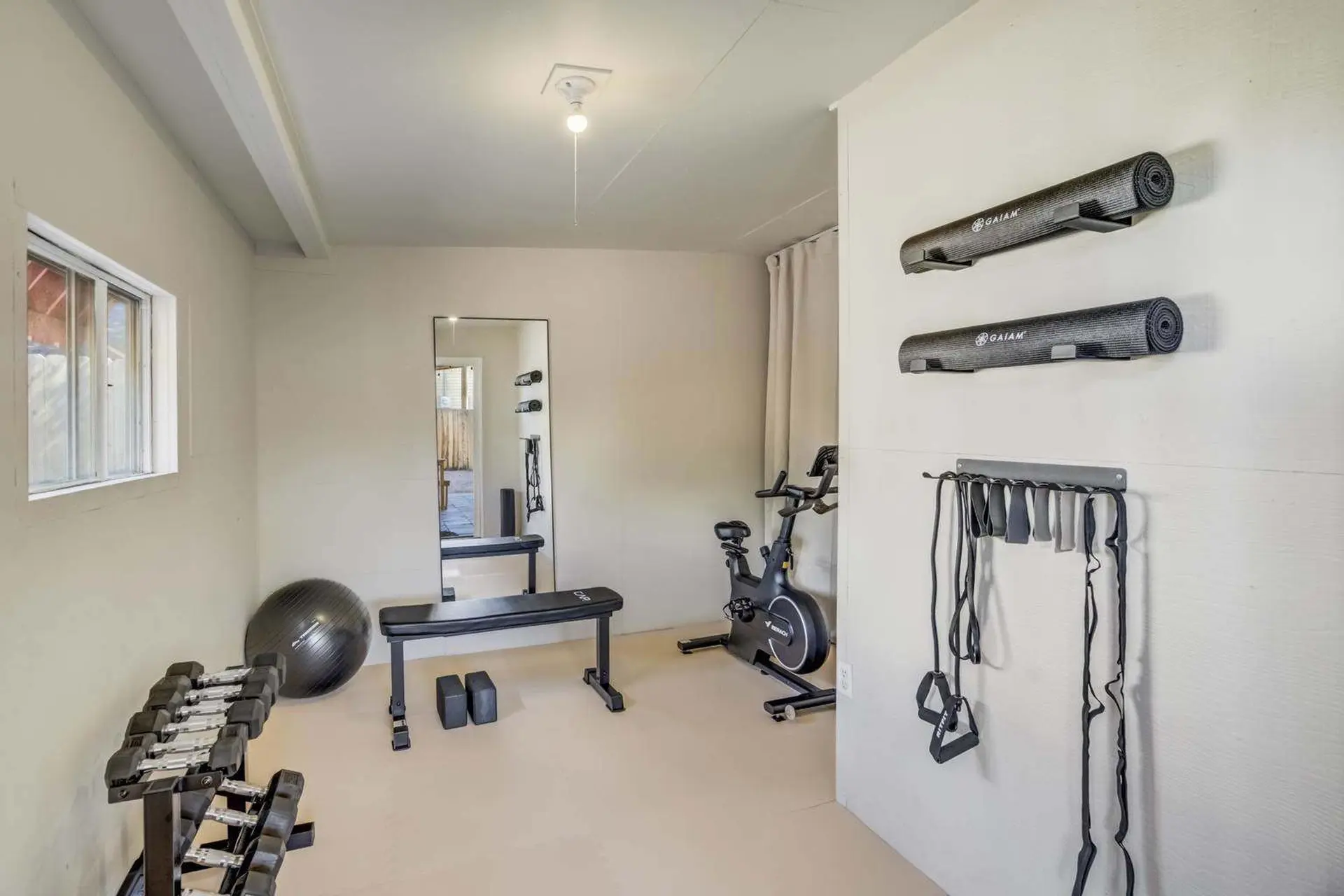 Home gym with exercise bike, weights, yoga mats, and resistance bands.