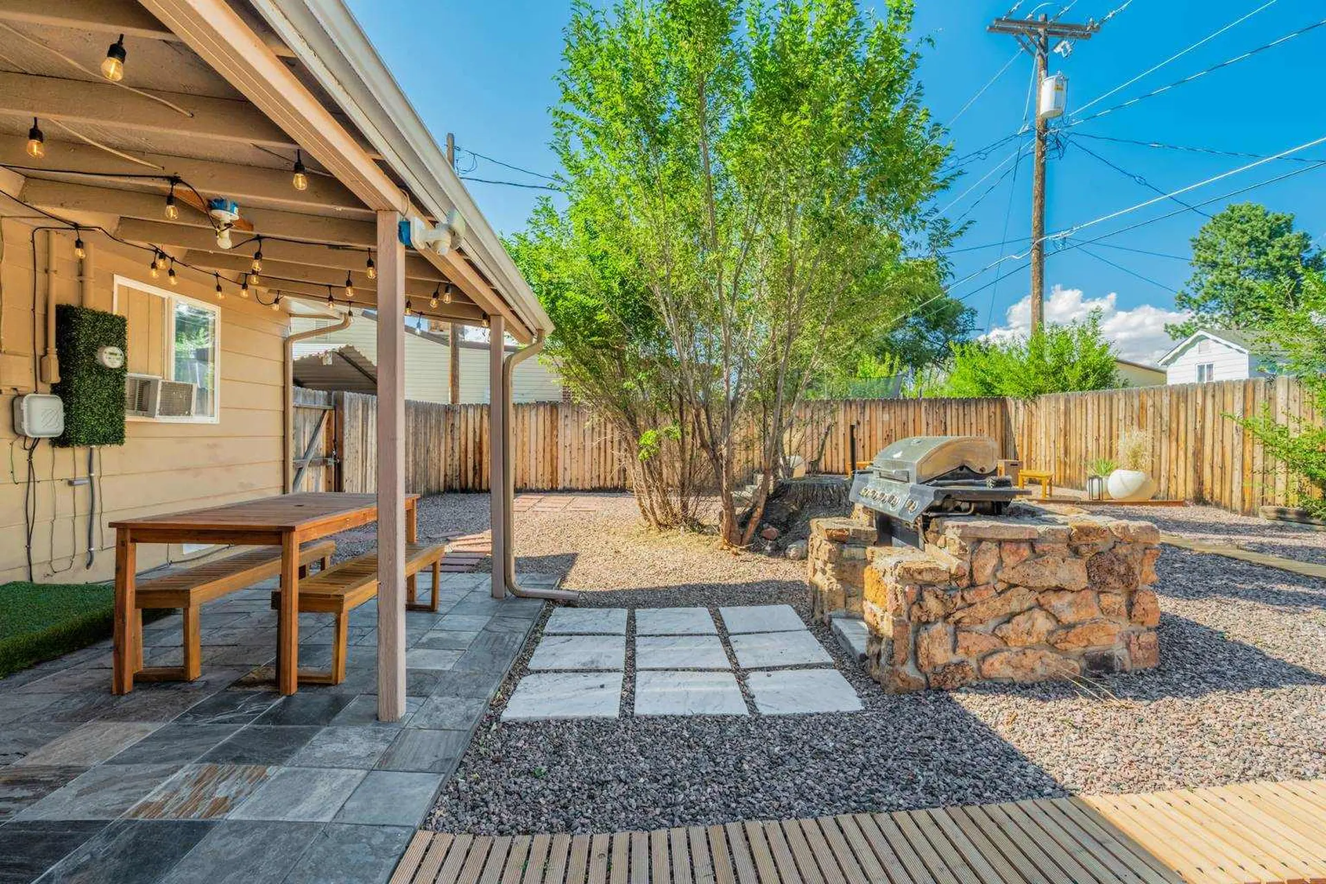 A backyard patio with a grill, dining table, and wooden fences.