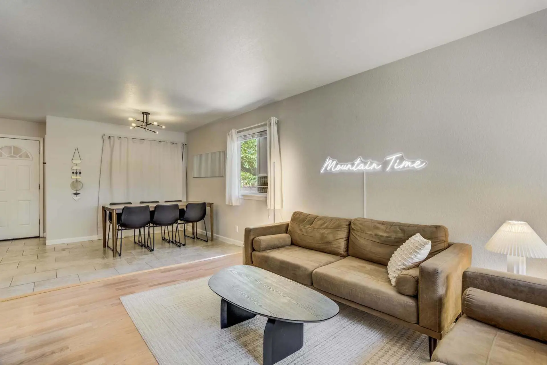 Living room with a couch, coffee table, dining table, and a neon sign that reads "Mountain Time".