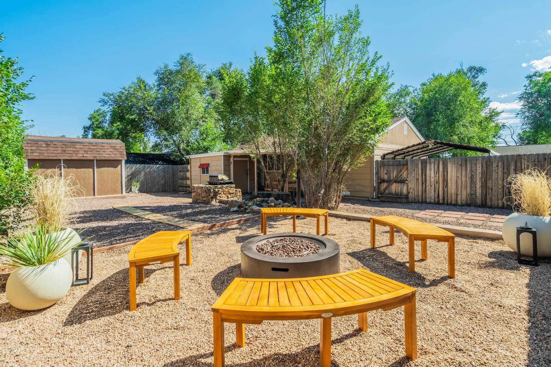 Backyard with fire pit, wood benches, and two sheds.