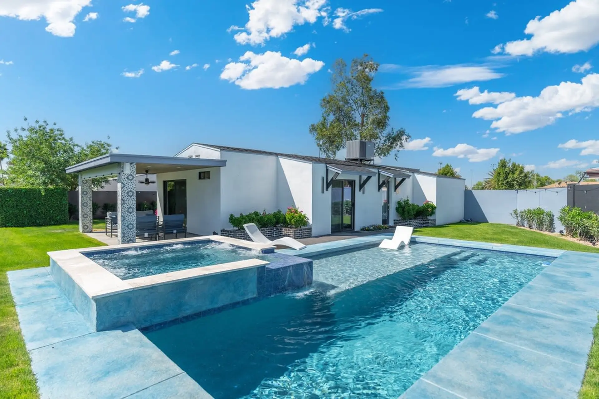 A modern house with a pool and spa, covered patio and lush green lawn.
