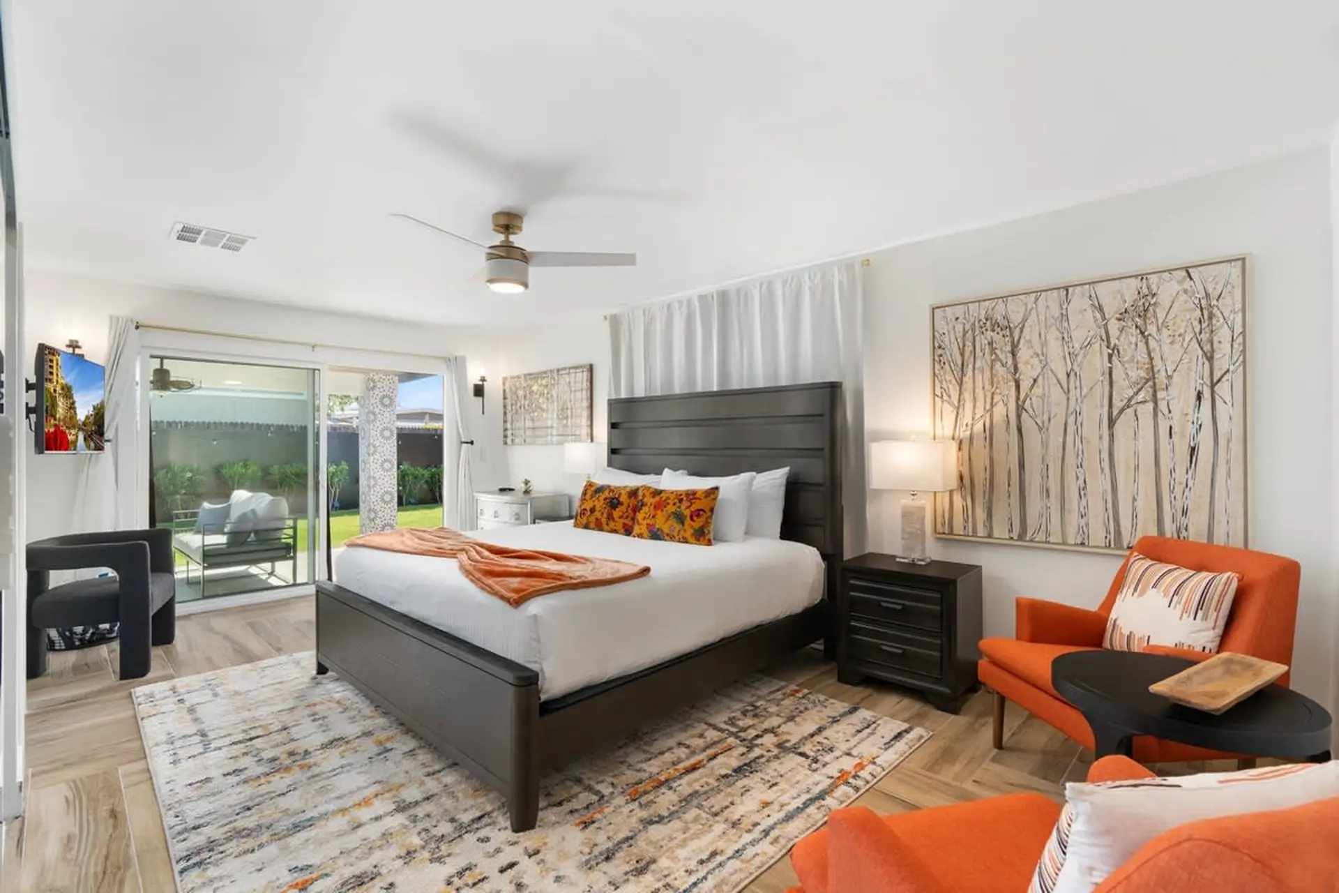 A bedroom with a king-size bed, orange chairs, and a large tree painting.